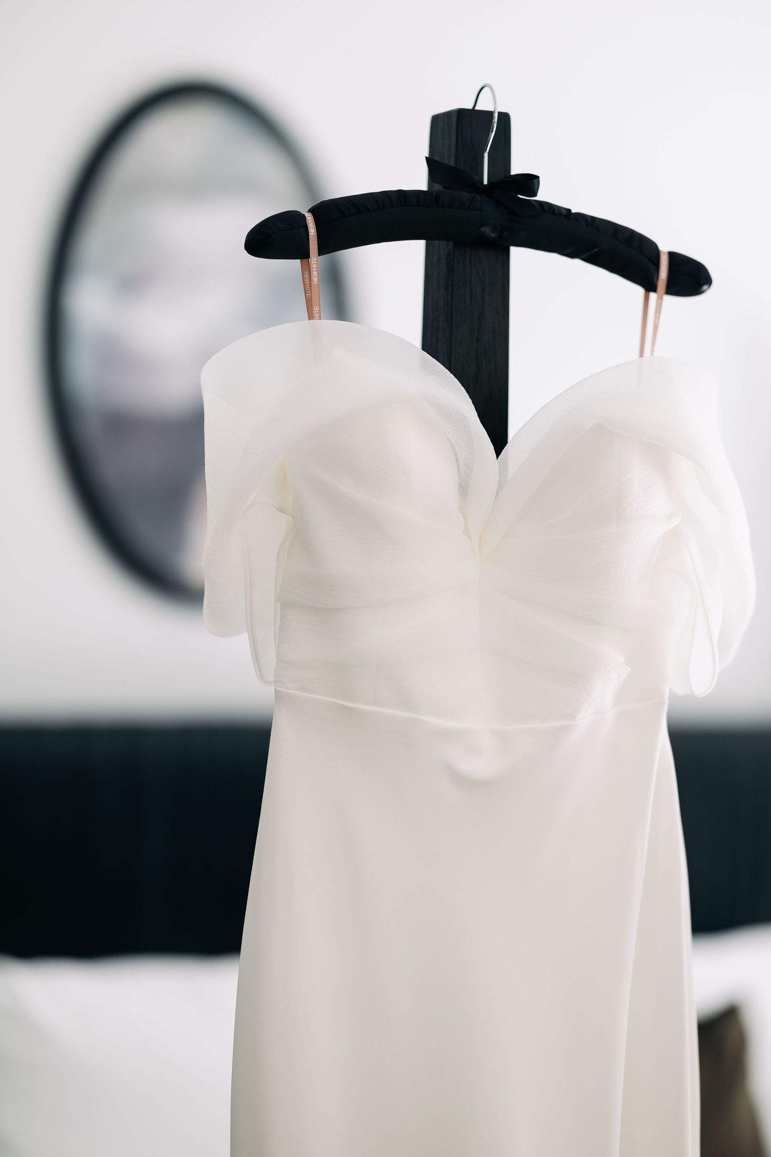 White wedding dress on a hanger displayed against a light background with clocks.