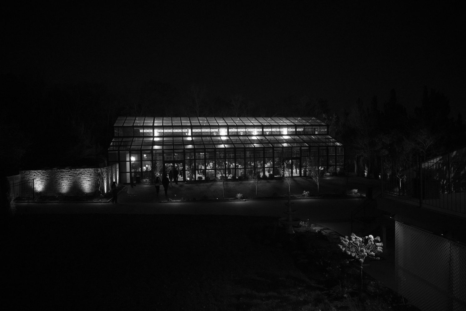 Illuminated glass greenhouse venue glowing against the dark night sky during an evening wedding reception.