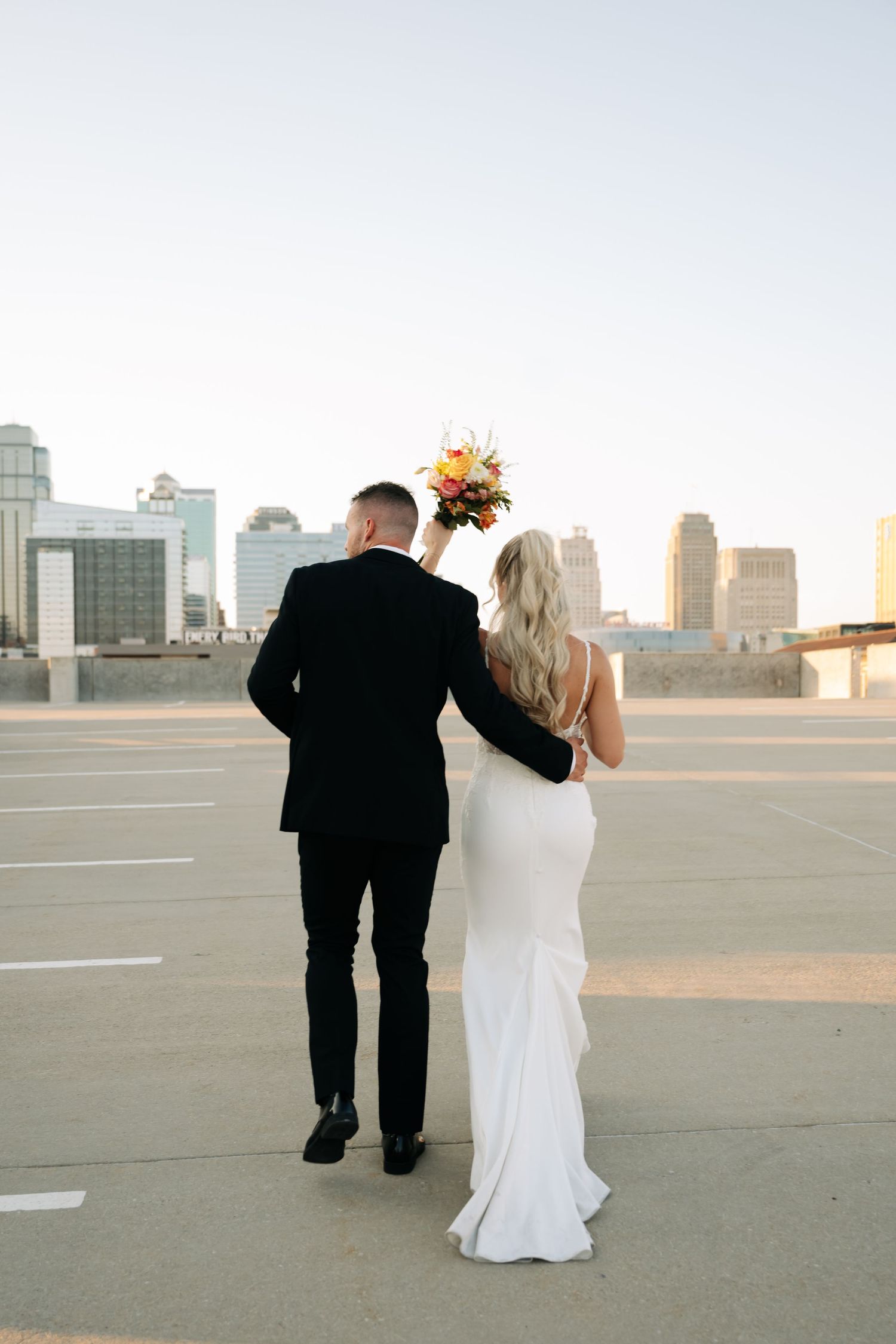 Wedding couple walking together on urban rooftop with the Kansas city skyline view.