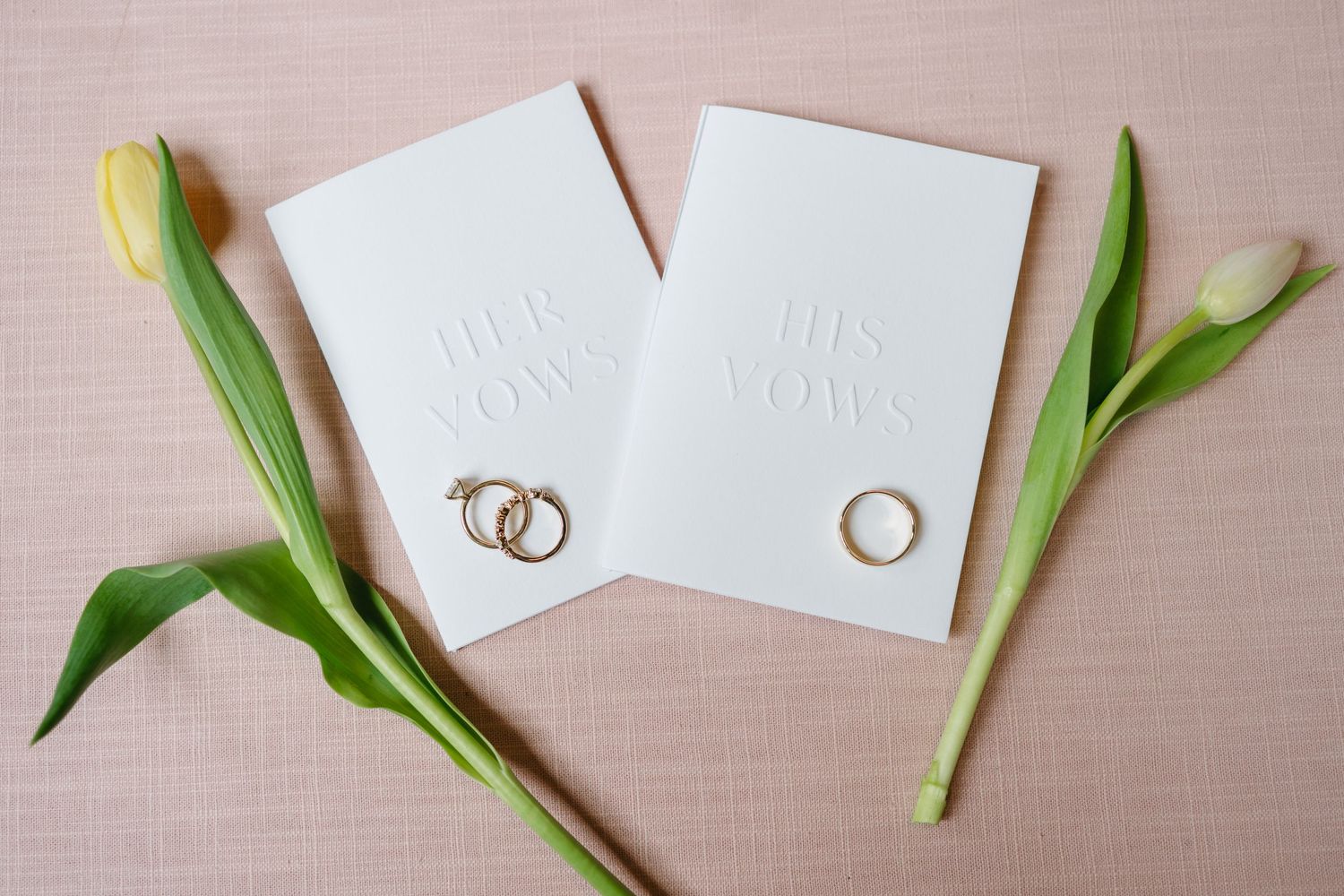 White wedding stationery and green tulips arranged on a light pink linen background.