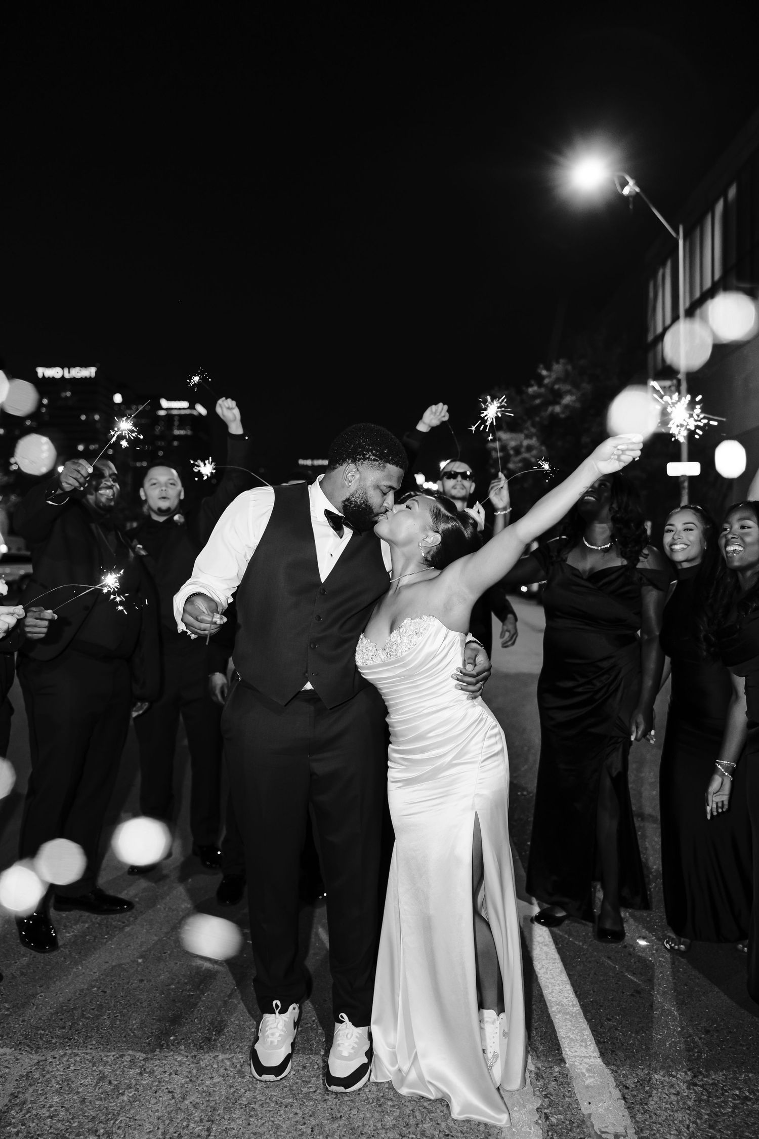 A couple celebrates their wedding night dancing outdoors surrounded by guests holding sparklers in black and white.