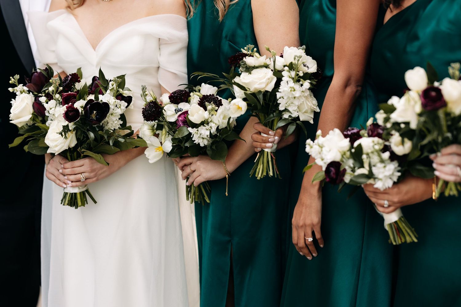 Wedding party holding white and green bouquets wearing emerald green dresses.