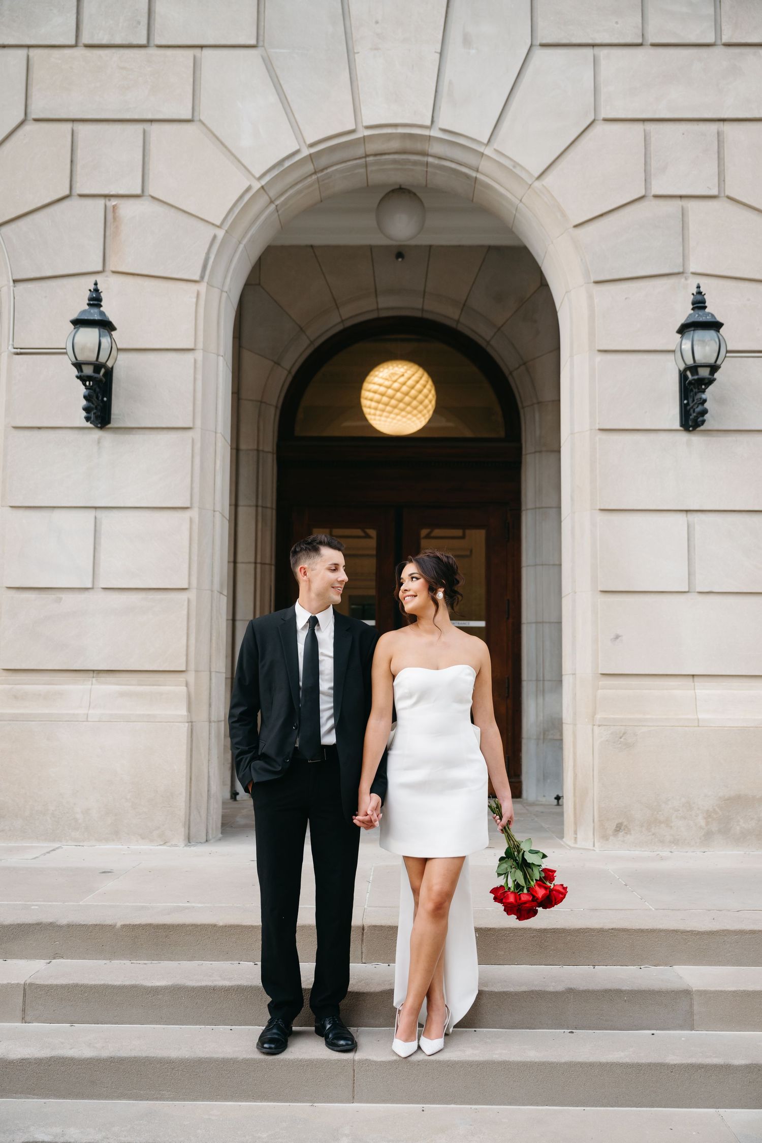 A wedding couple poses in front of a grand stone archway entrance.