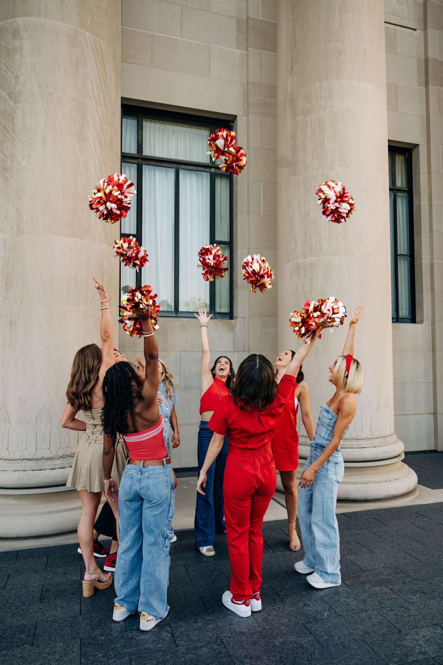 Group of Chiefs cheerleaders in red and denim outfits performing with pom poms against a stone column backdrop.