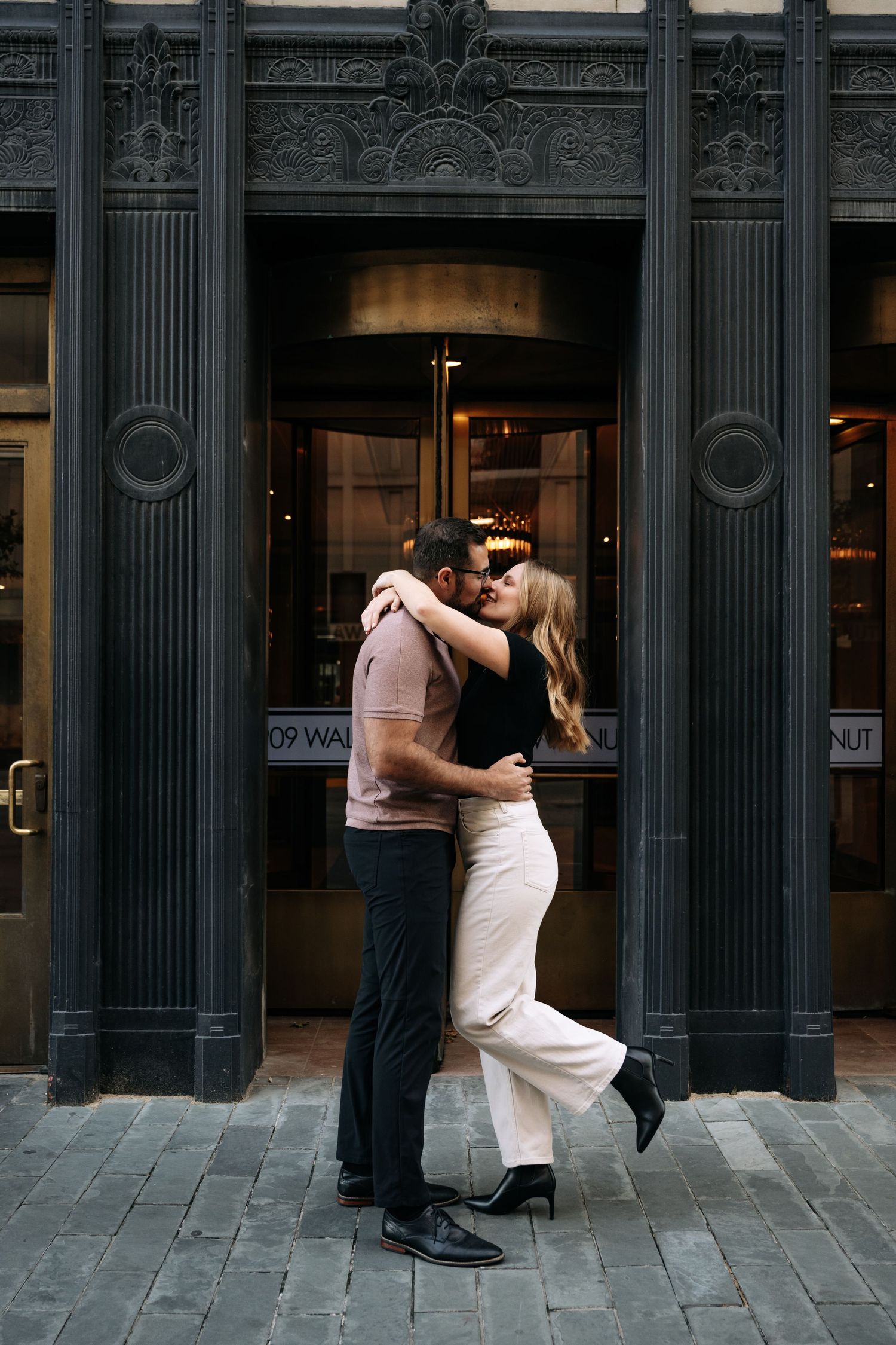 A couple dances and embraces against a classic stone building facade.