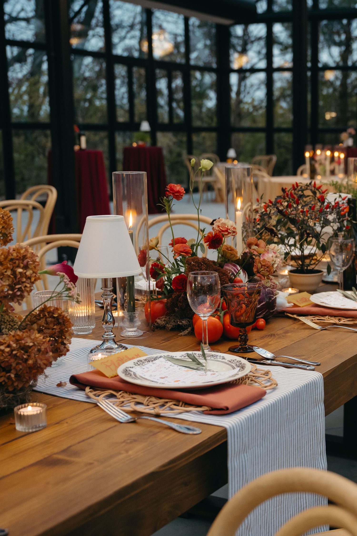 Rustic wooden table set with red floral centerpieces and elegant place settings for a wedding reception.