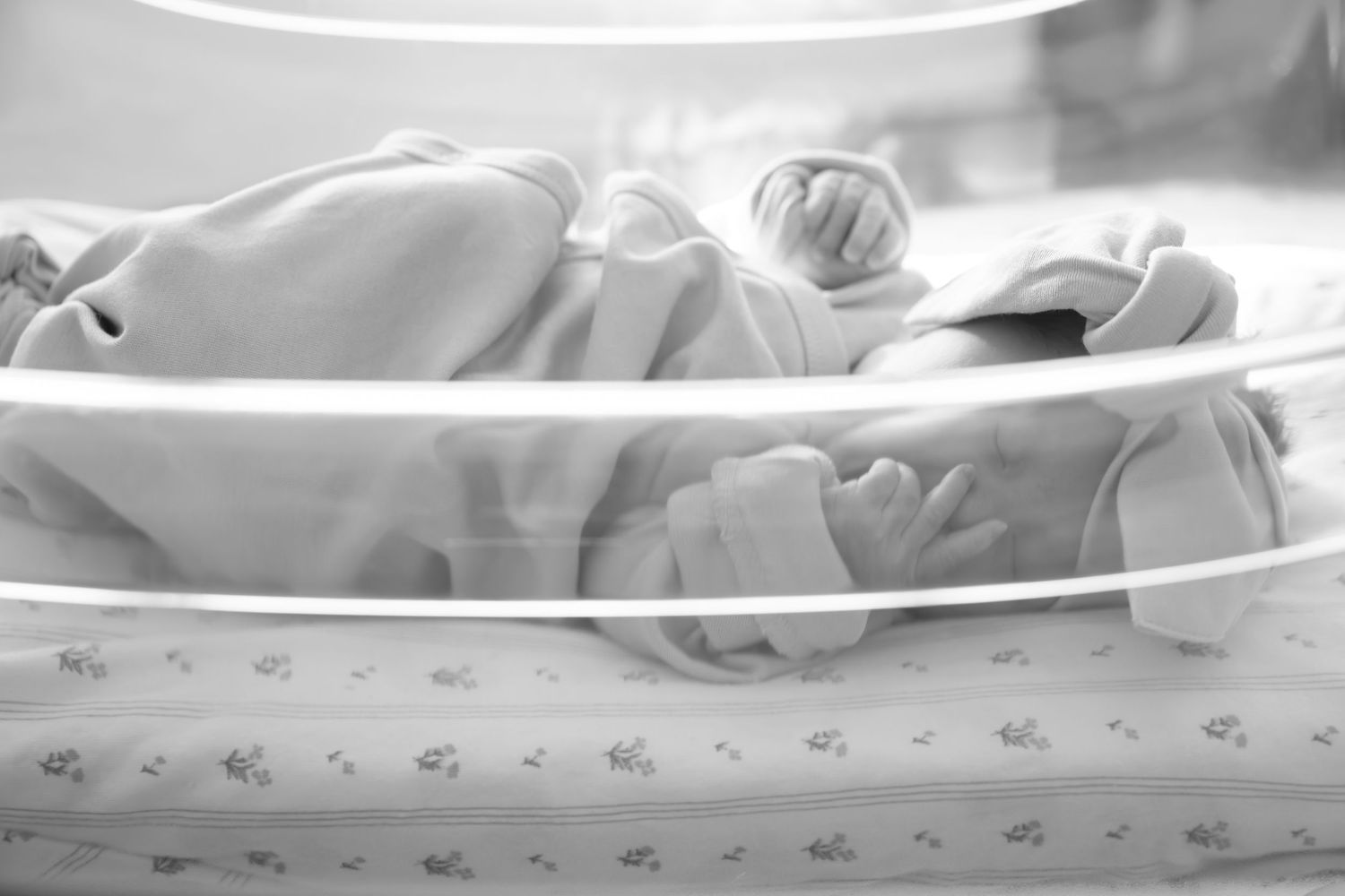 Peaceful newborn baby sleeping under soft white blanket in gentle lighting.