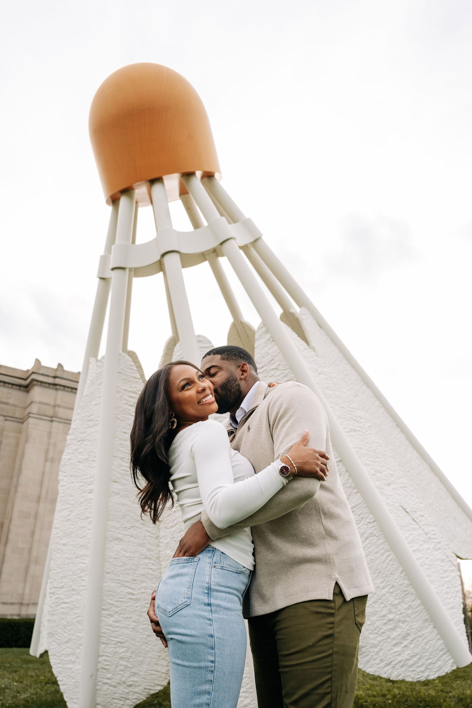 Couple embracing under large white sculptural art installation.