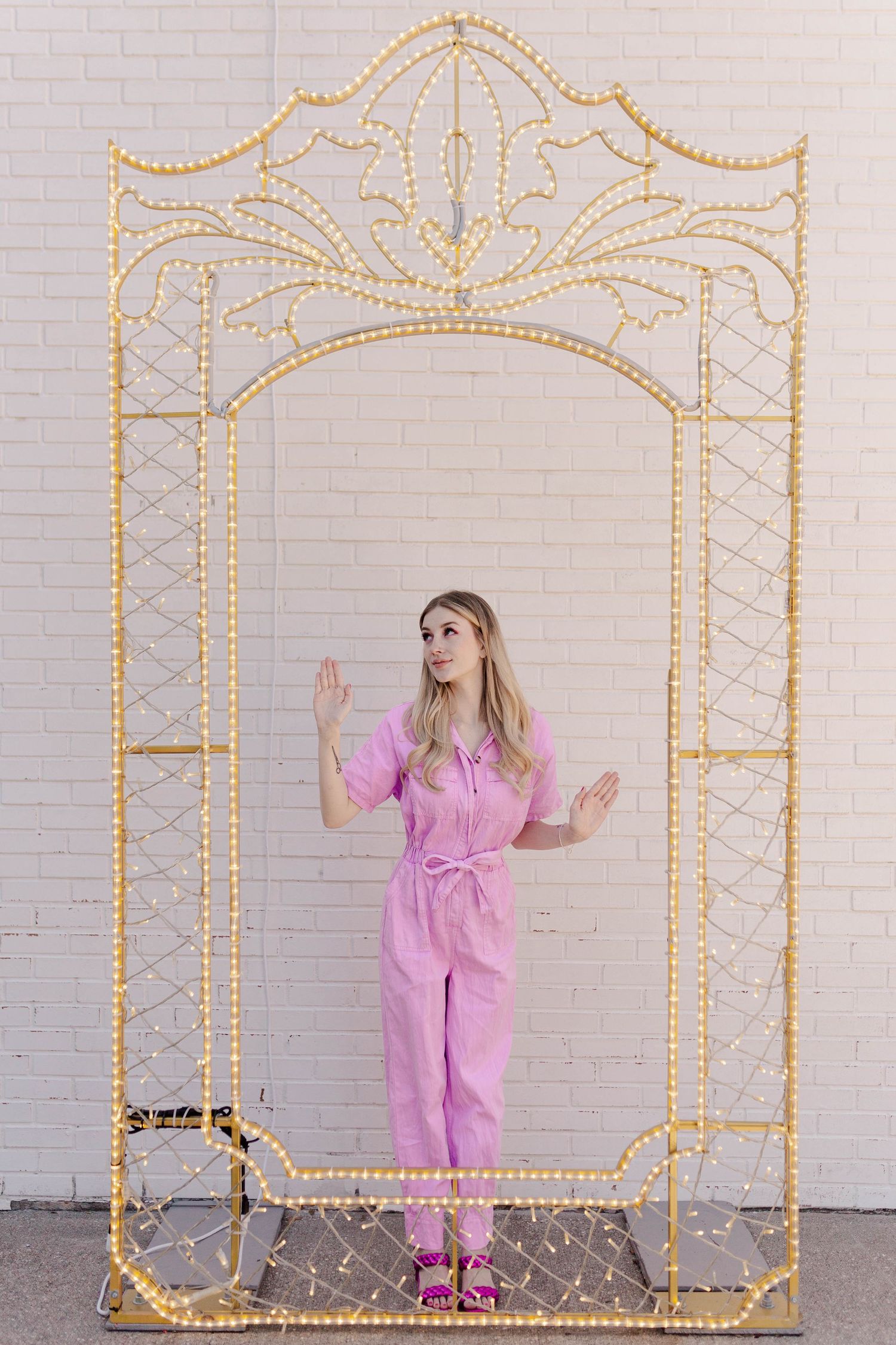 blonde model posing as barbie in pink coveralls in front of a white brick wall in Houston Texas