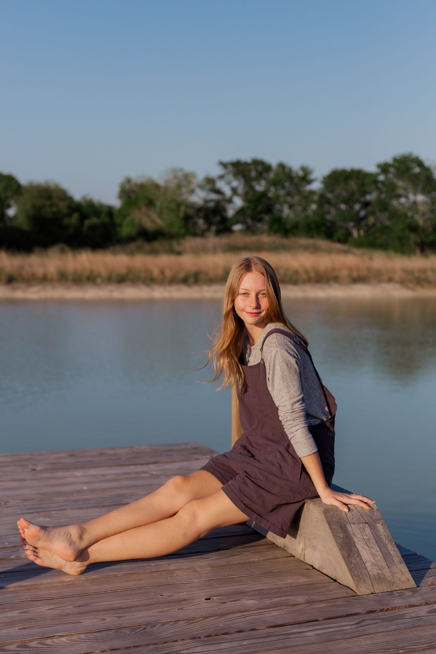 blonde white high school senior girl poses on a pier in a pond in Alvin Texas for photoshoot
