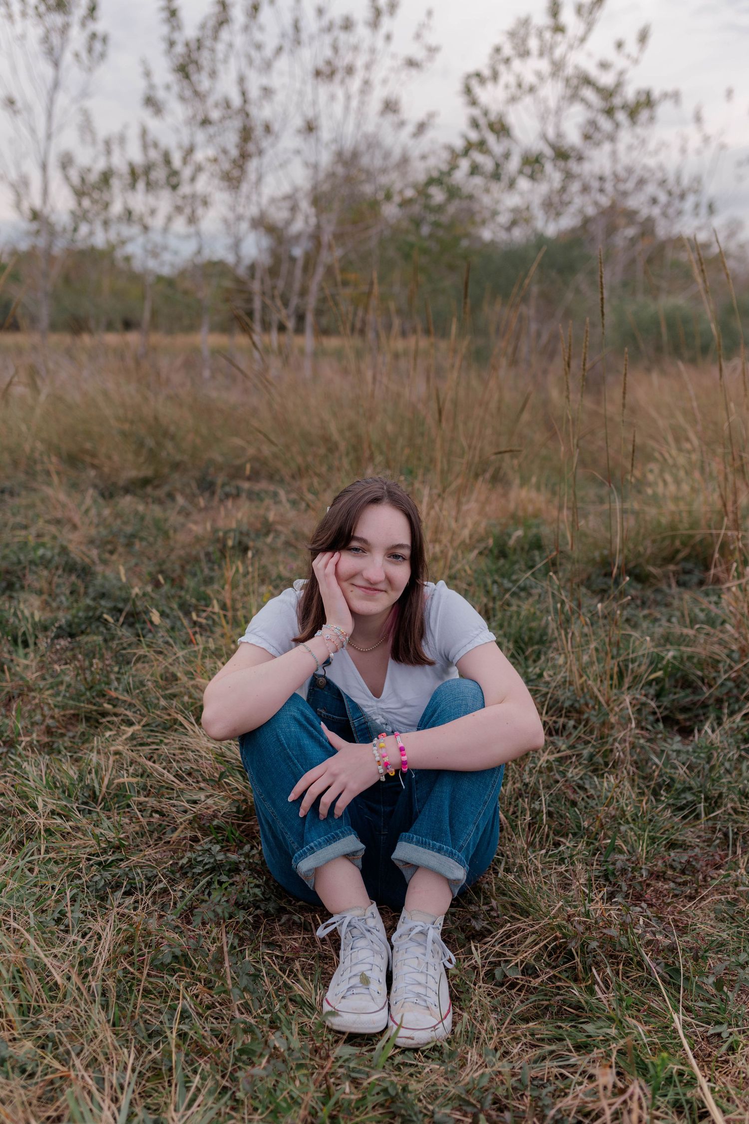 high school senior girl sits in field of dying grass at a park in friendswood Texas for highschool senior photos