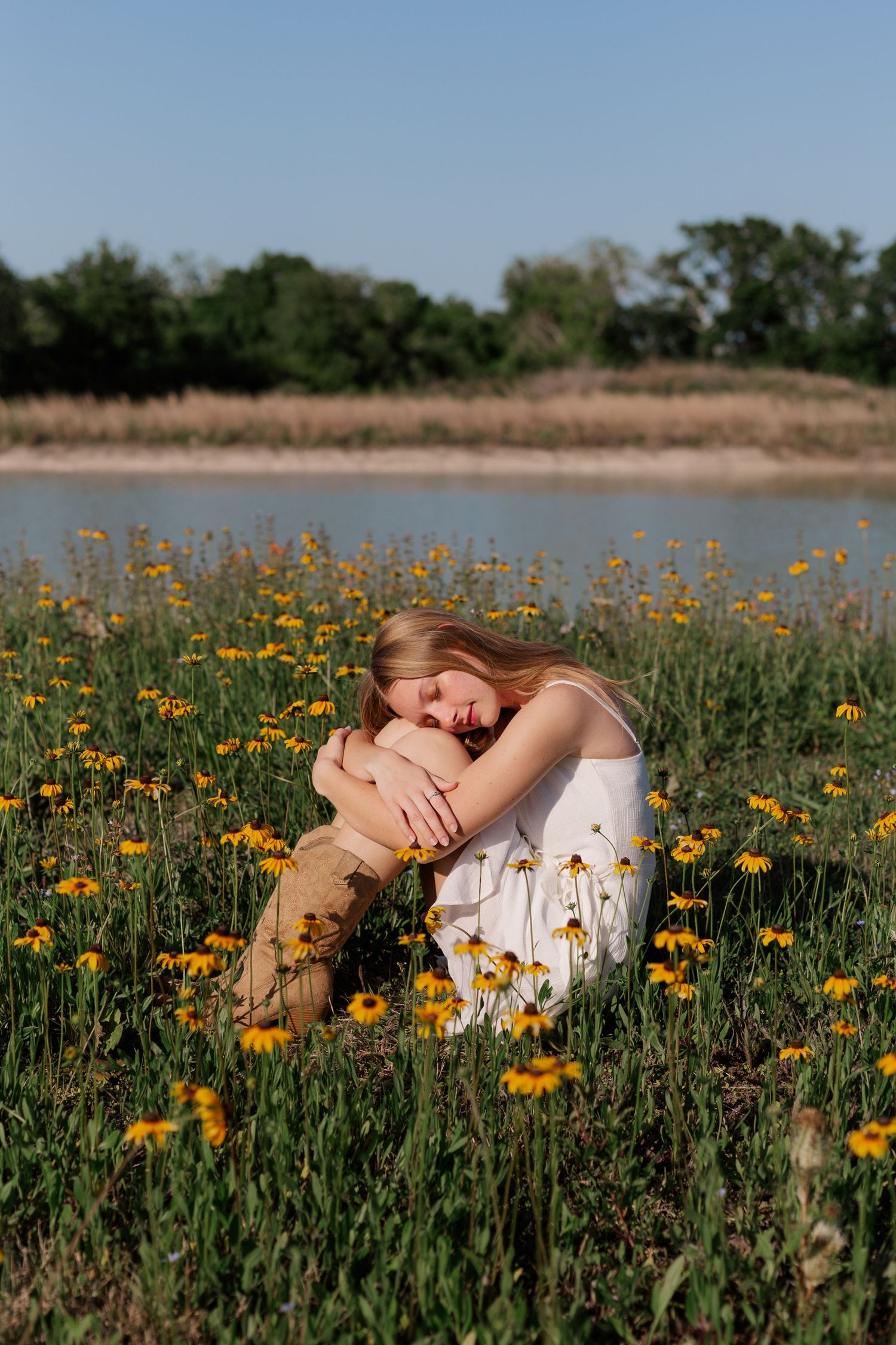 white blonde high school senior girl sits in front of pond at sunset for senior photos