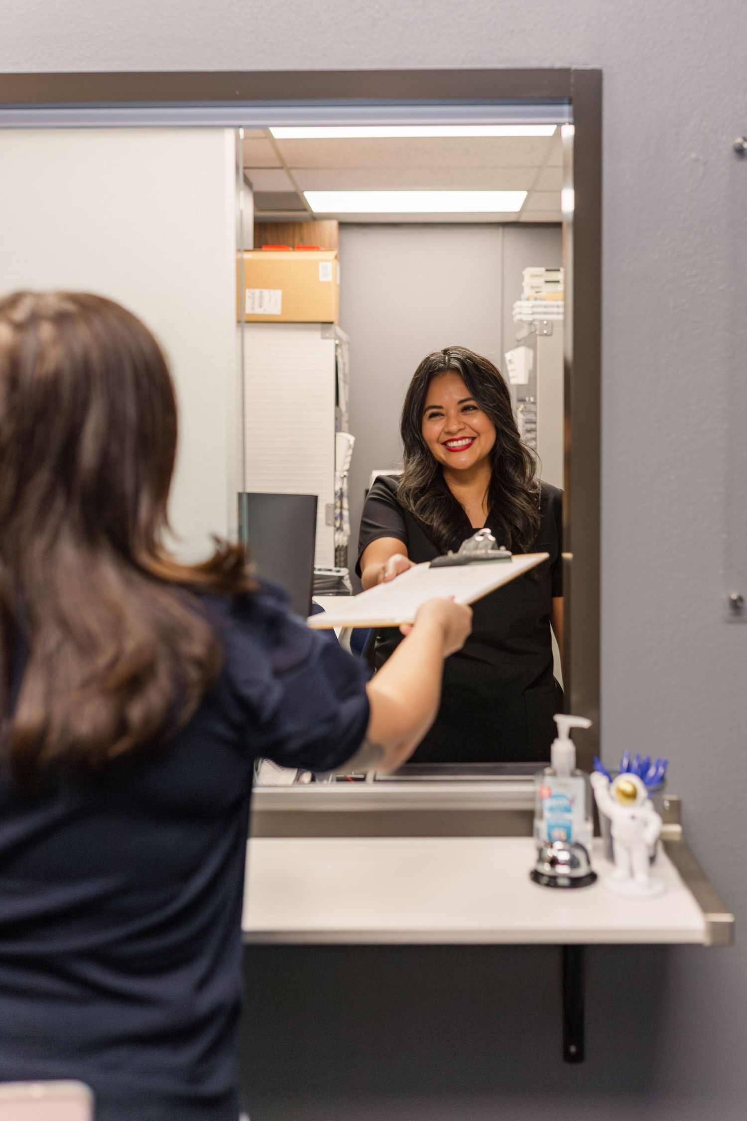 hispanic woman offers white woman a form on a clipboard at a doctors office for business branding photoshoot