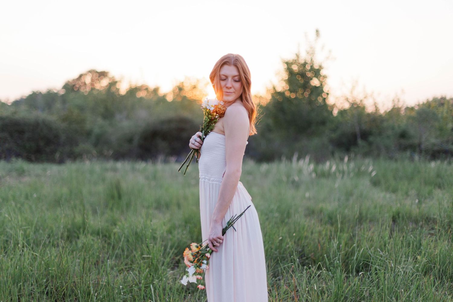 high school senior girl poses in field at sunset with bouquet of flowers for senior photos in friendswood Texas park