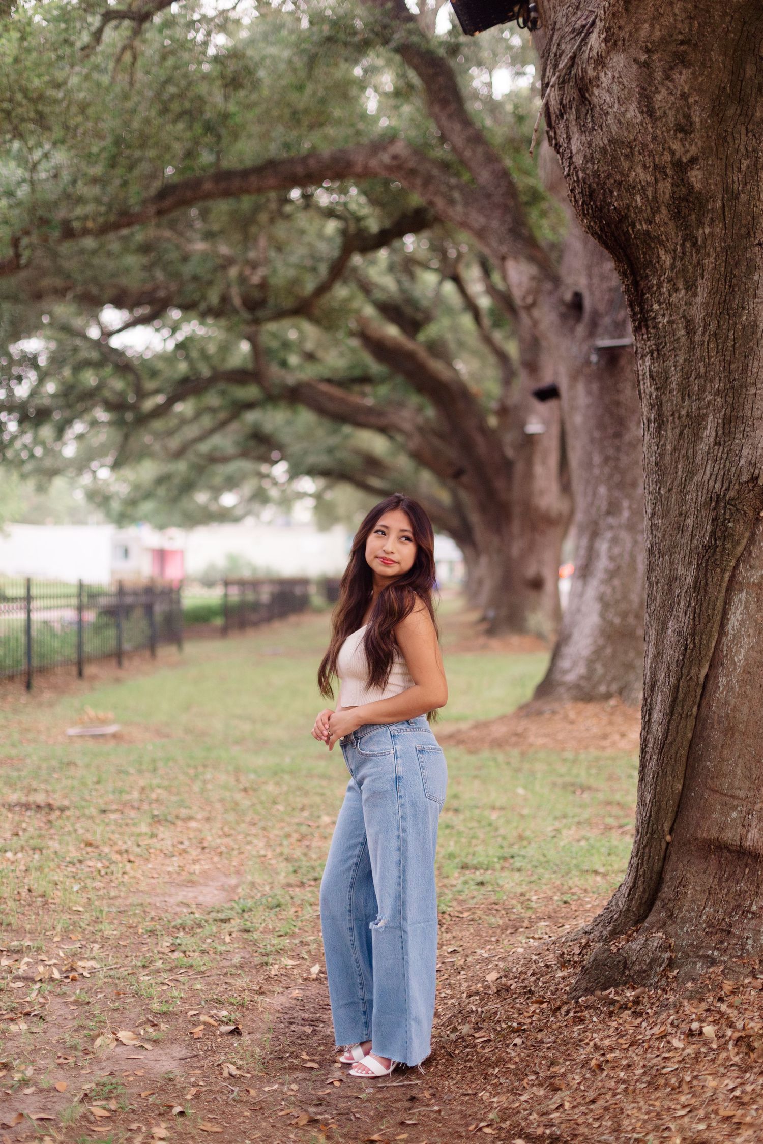 hispanic girl poses next to large oak trees in downtown league city Texas for highschool senior photos
