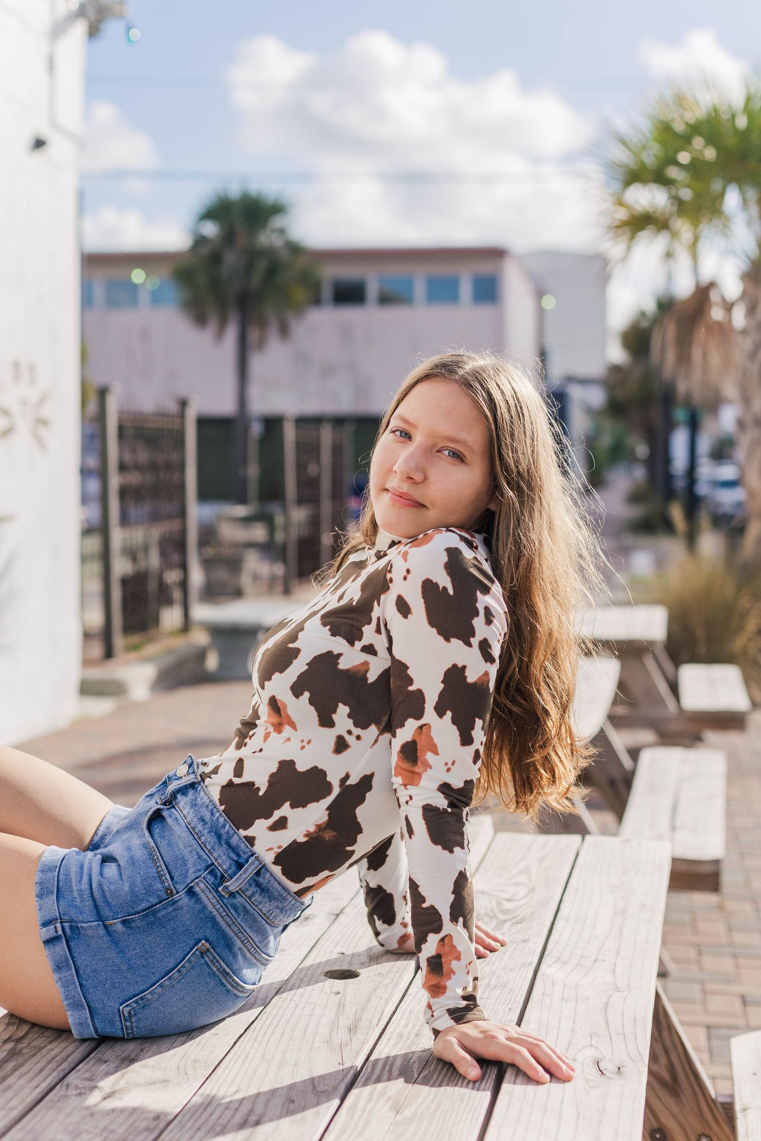 high school senior girl in cow print top sits on a picnic table in Galveston Texas posing for high school senior photos