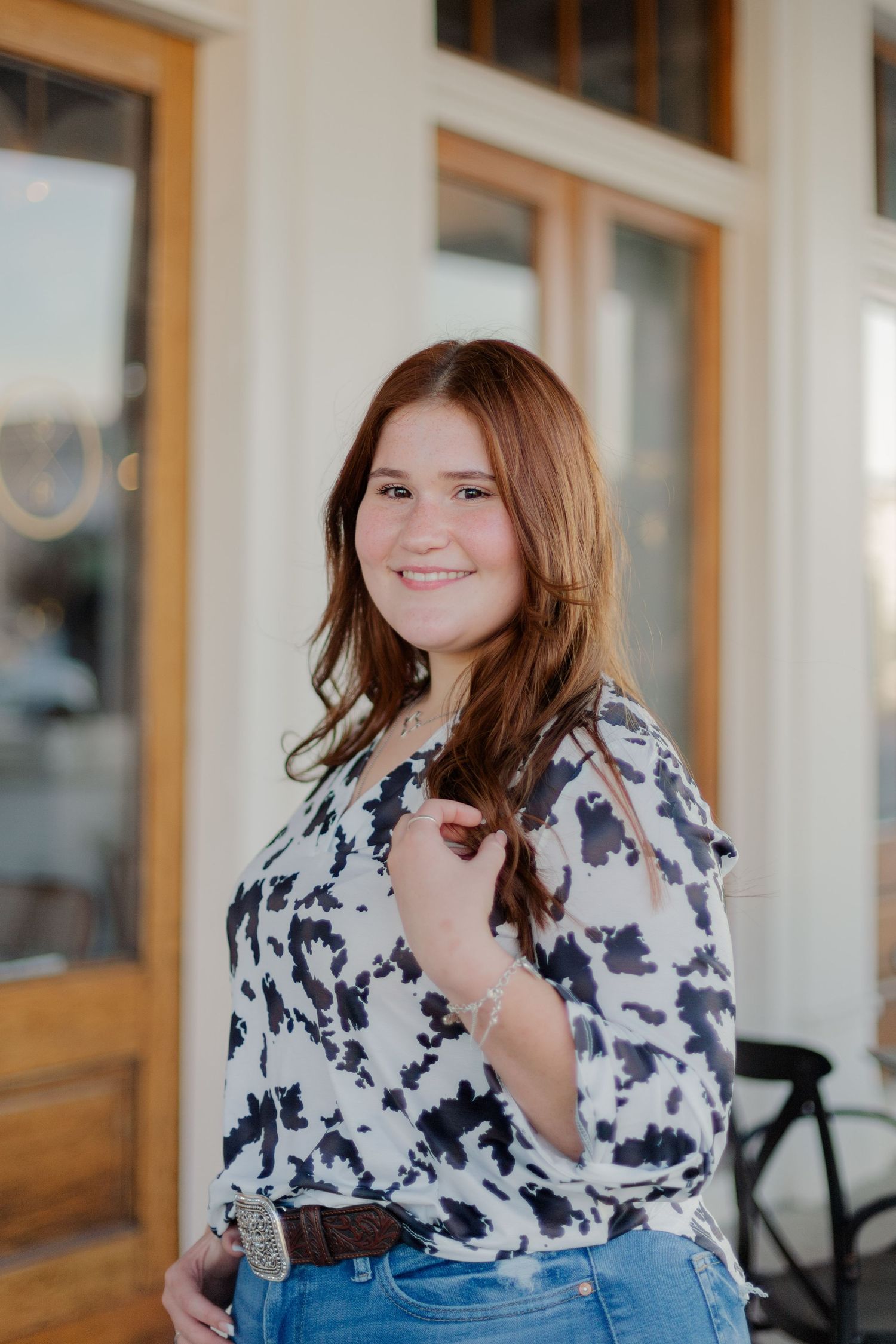 high school senior girl posing in front of restaurant in Galveston Texas with hand in hair for photo session smiling at the camera