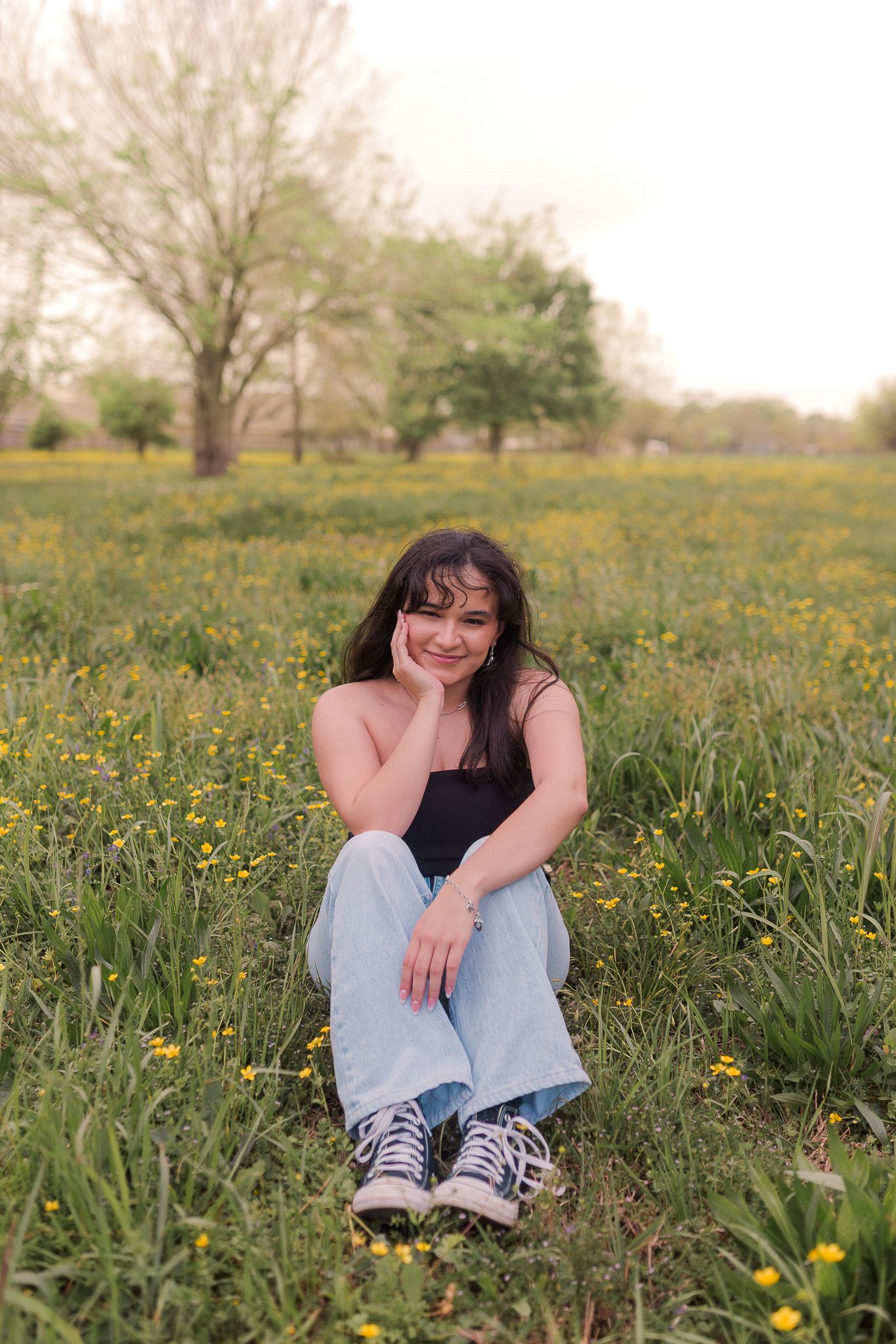 mexican high school senior girl sits in field of yellow wildflowers and smiles for senior photos in league city Texas