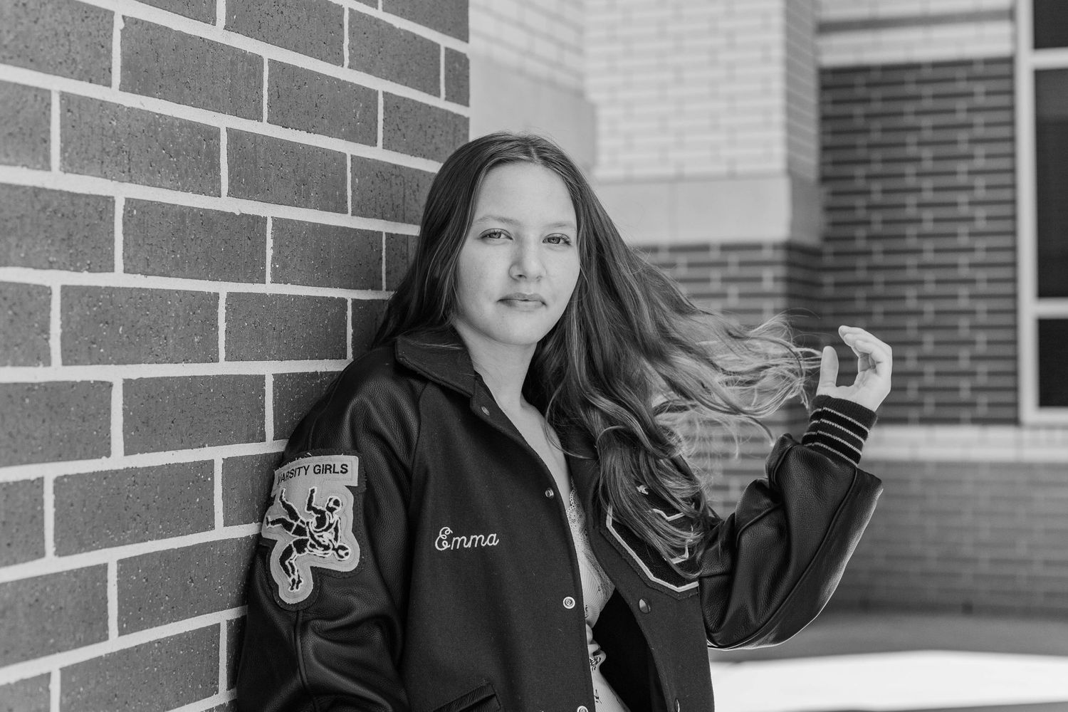 black and white photo of a girl posing in letterman jacket in front of clear springs high school in league city Texas