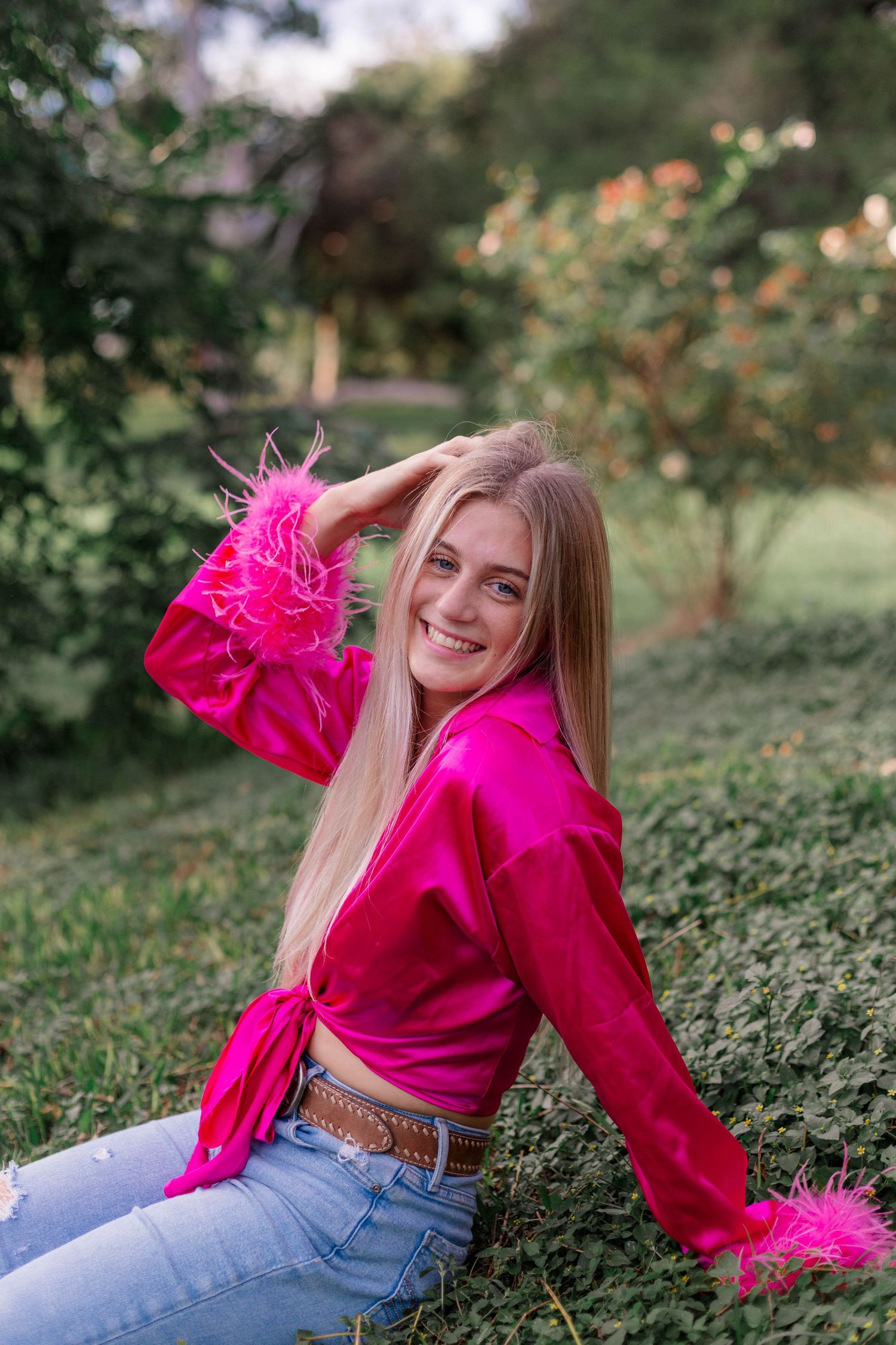 blonde white high school senior girl poses on a small hill in a hot pink top for senior pictures