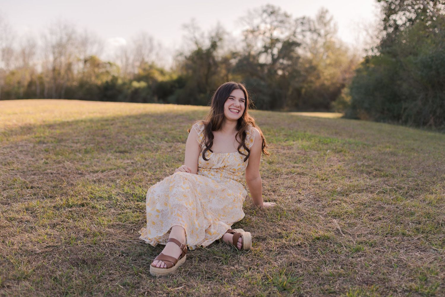 highschool senior girl poses on a small green hill at sunset in a park in friendswood Texas for senior photos