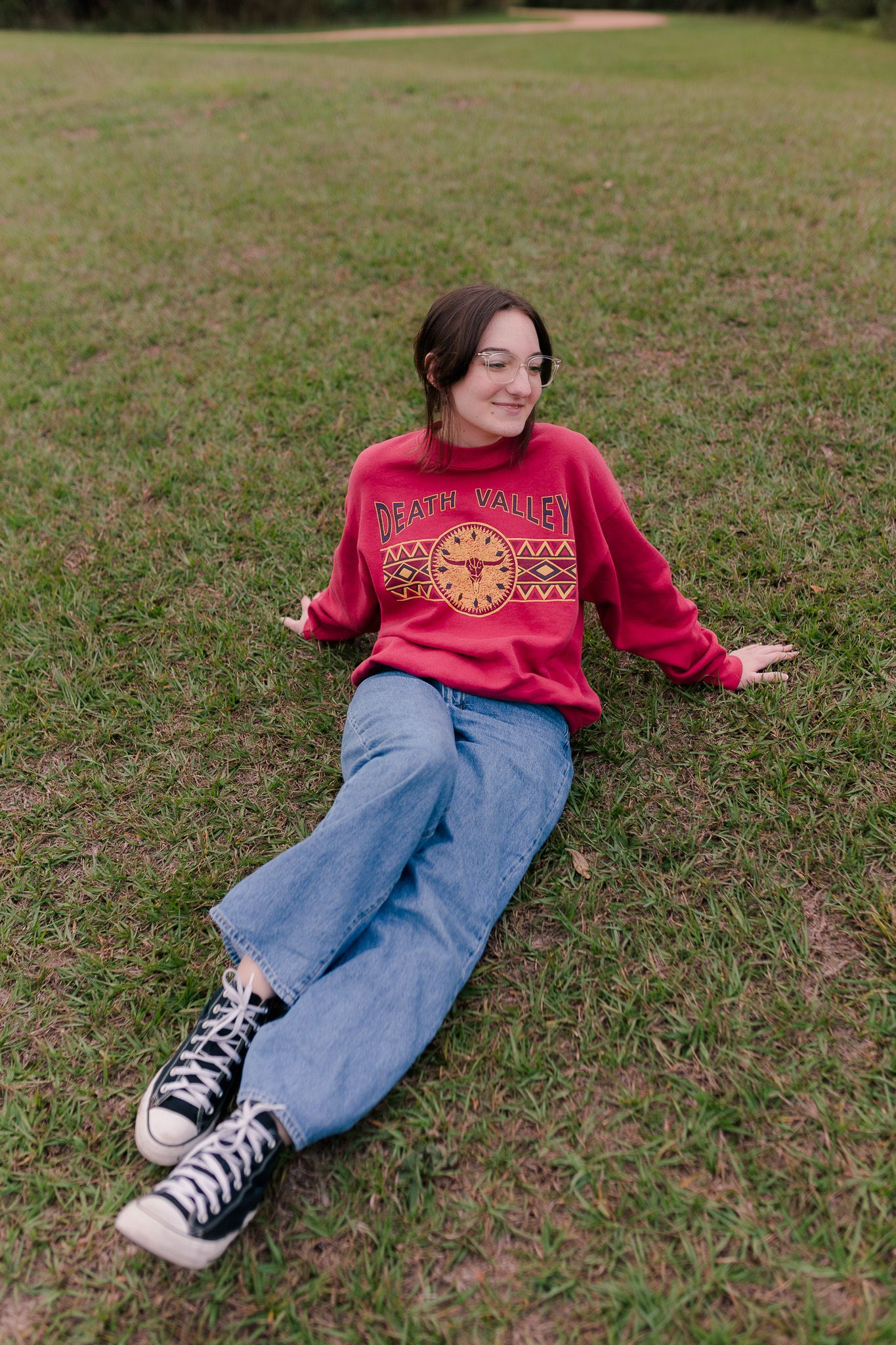 high school senior girl sits in grass and poses for senior photos at a park in friendswood Texas