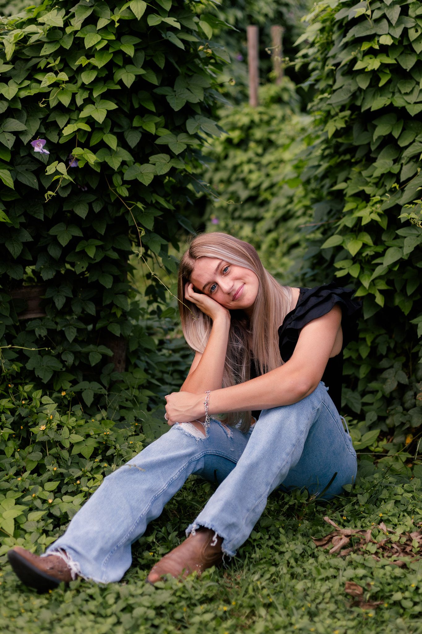 high school senior girl hugs knees and poses with a large green vine for high school senior photos in Alvin Texas