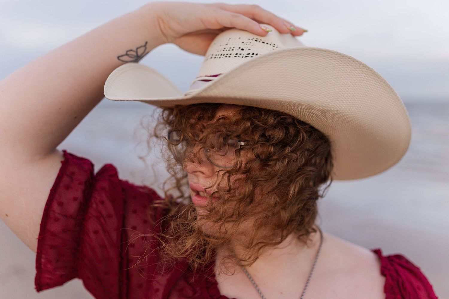 white girl with curly red hair poses with a cowboy hat for high school senior photos in seabrook Texas