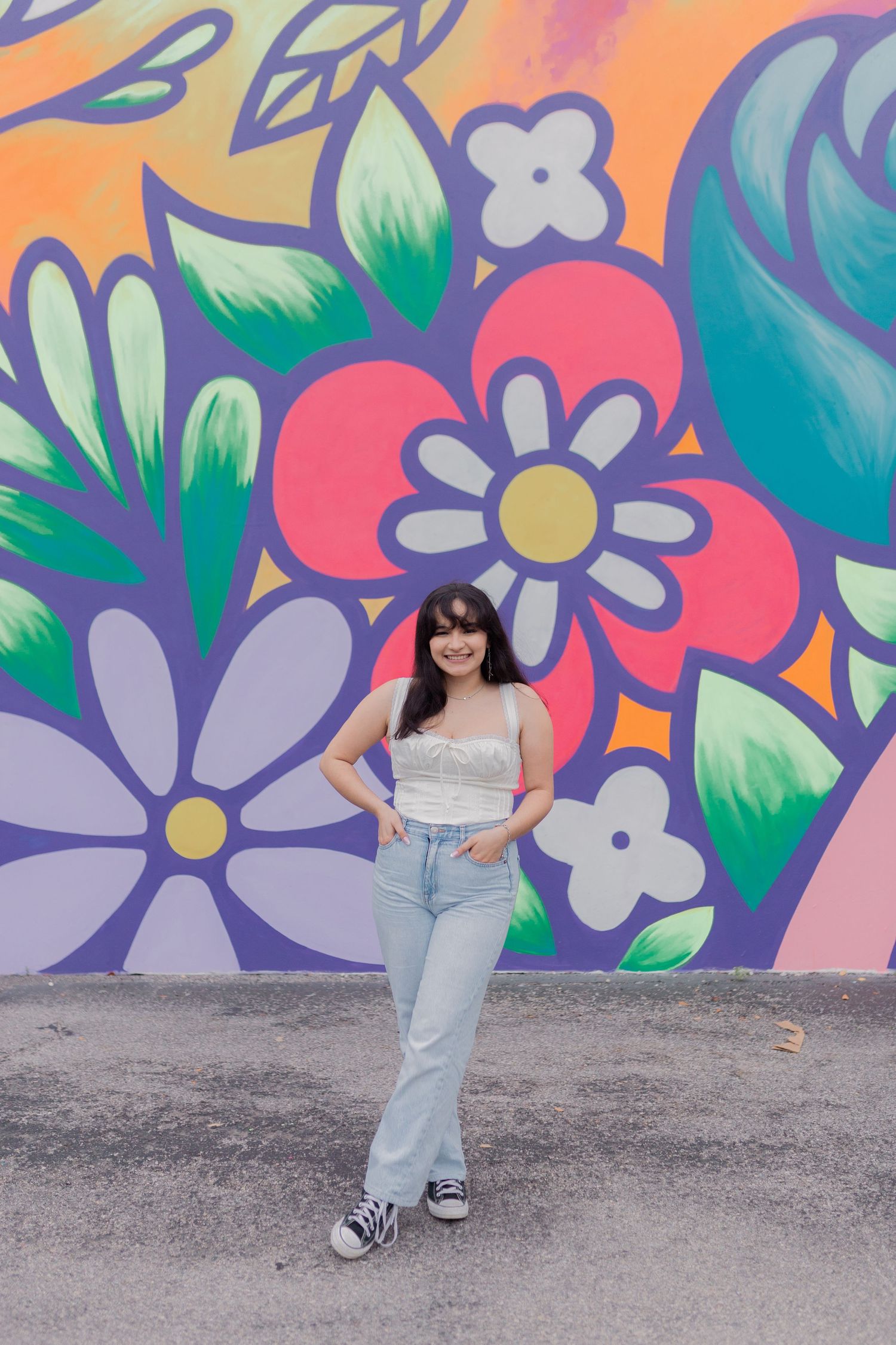 Mexican high school senior girl stands in front of a cartoon floral mural in friendswood Texas for high school senior photos