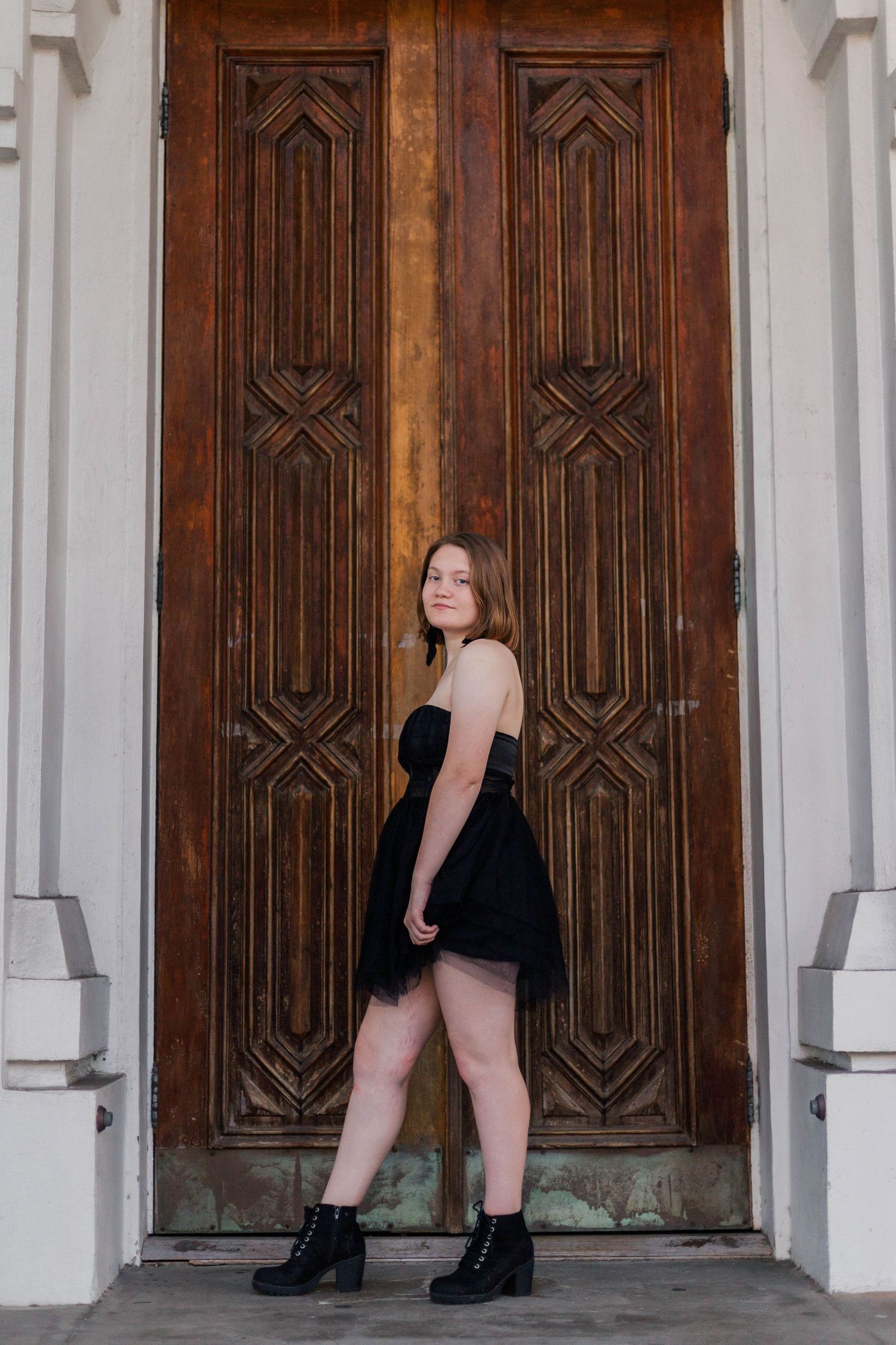 white girl in black dress and clogs stands in front of large wood door of a Catholic Church on broadway street in Galveston Texas