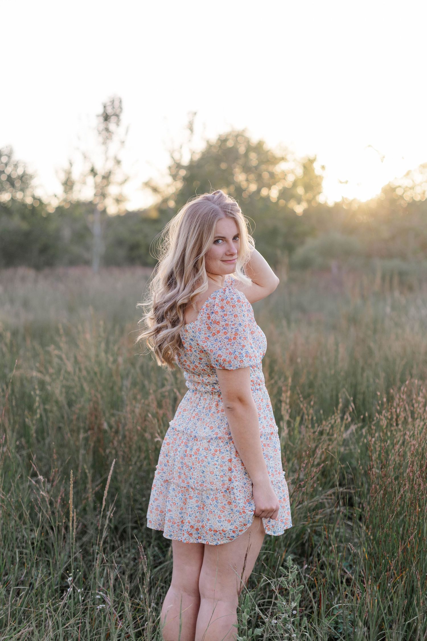 blonde white high school senior girl poses and smiles in a field at sunset in a park in friendswood Texas