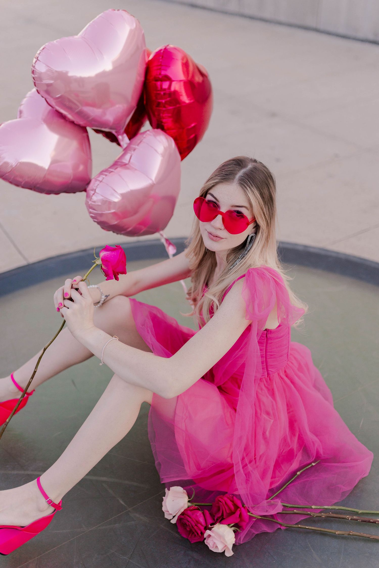 blonde model posing in a hot pink dress with pink heart shaped balloons at POST Houston with red and pink roses at a barbie theme photoshoot