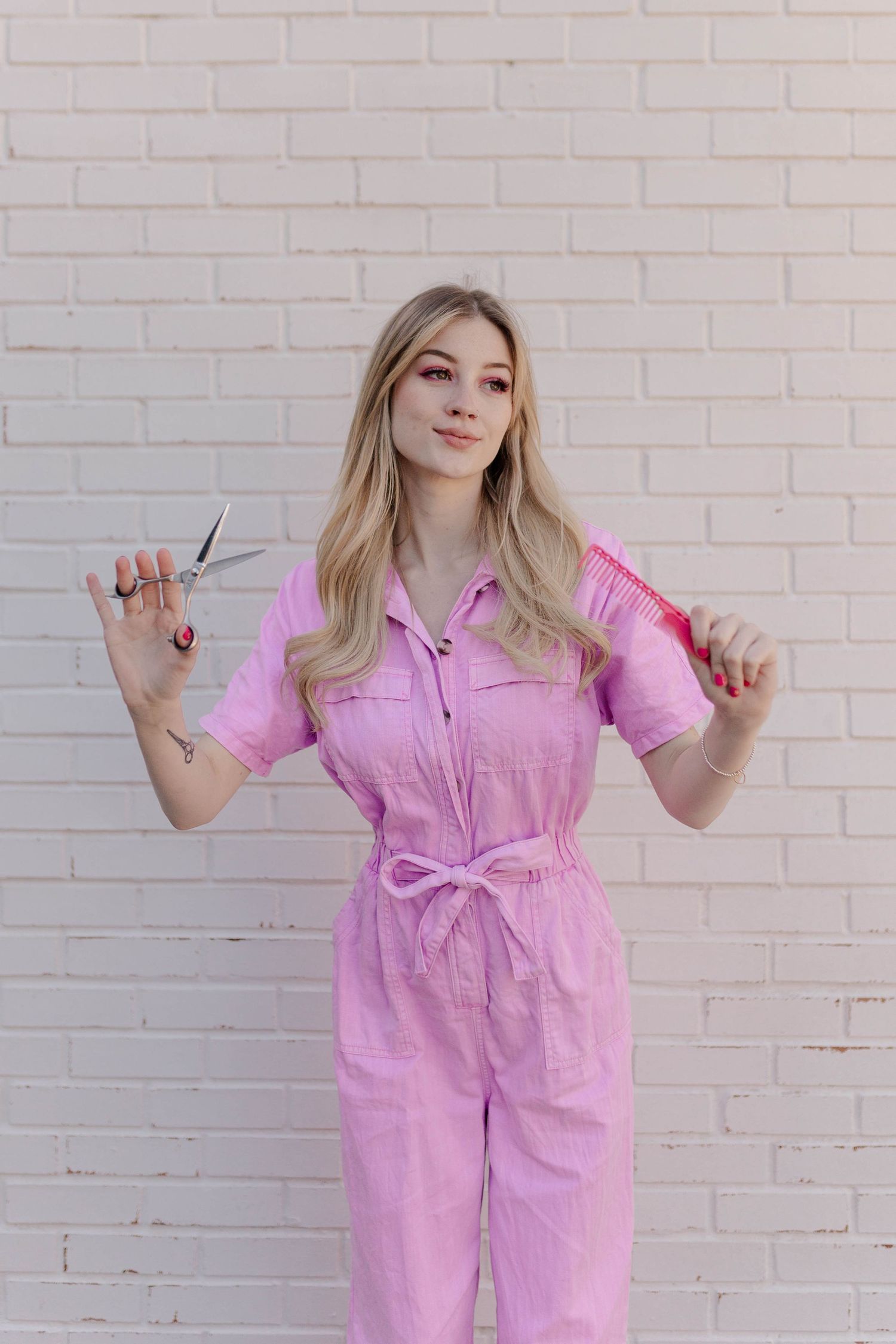 blonde model posing as barbie in pink coveralls in front of a white brick wall in Houston Texas