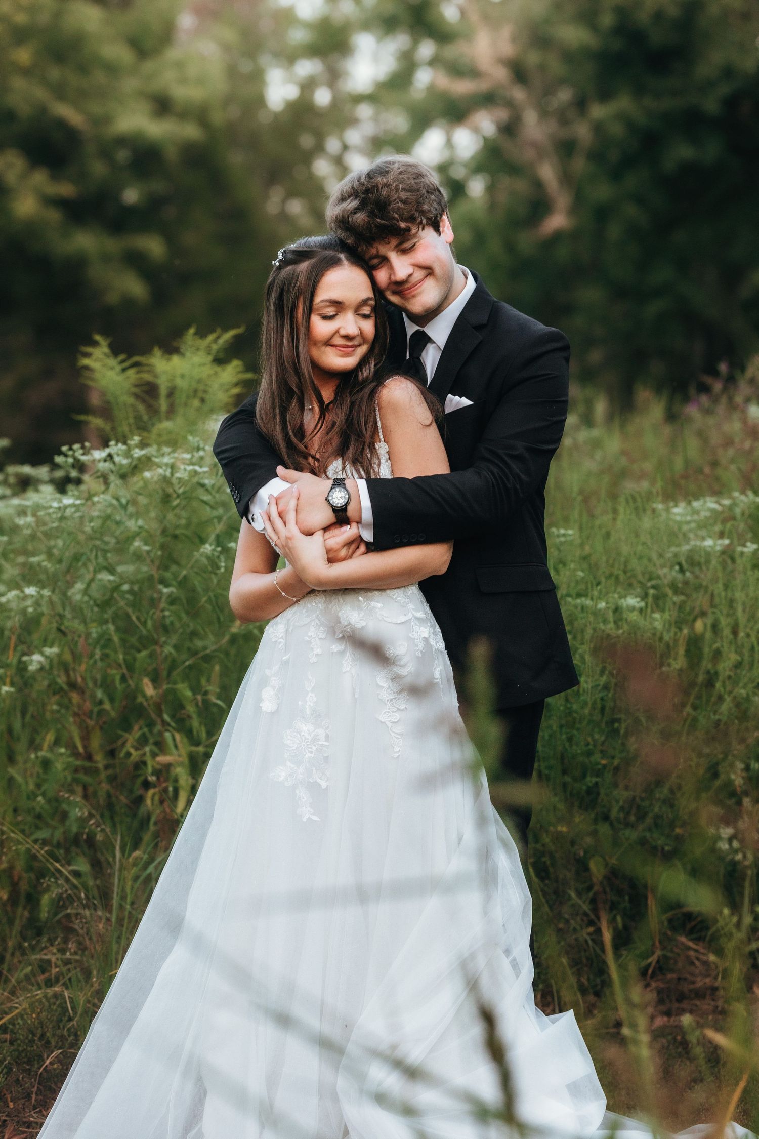 A tender moment between newlyweds embracing in a lush green meadow.