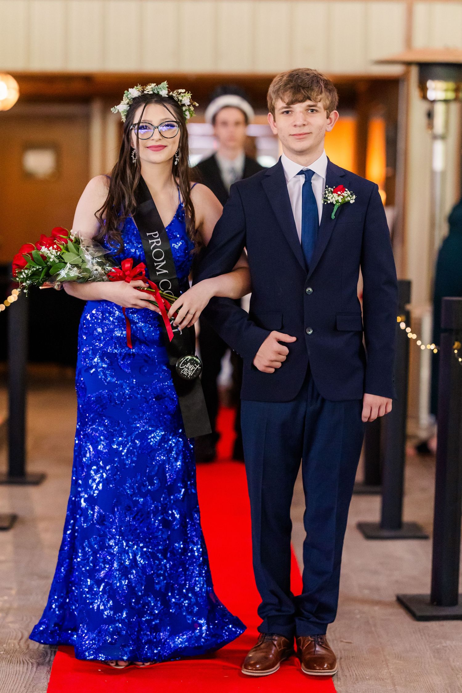 Couples in blue sequined dresses and dark suits pose on a red carpet at a formal event.
