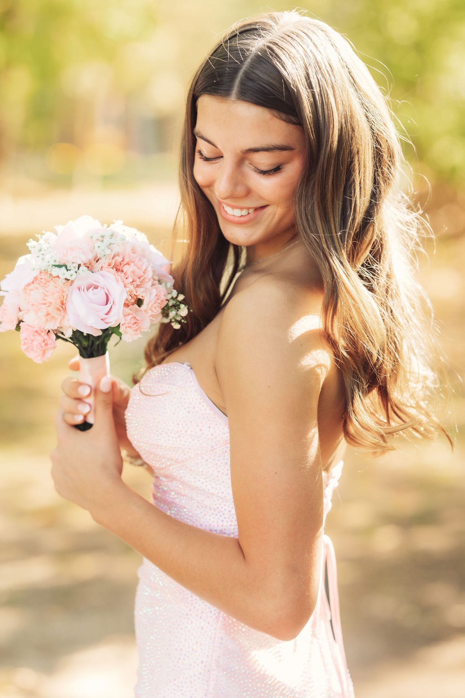 Pink floral bouquet held against formal dress in natural lighting.