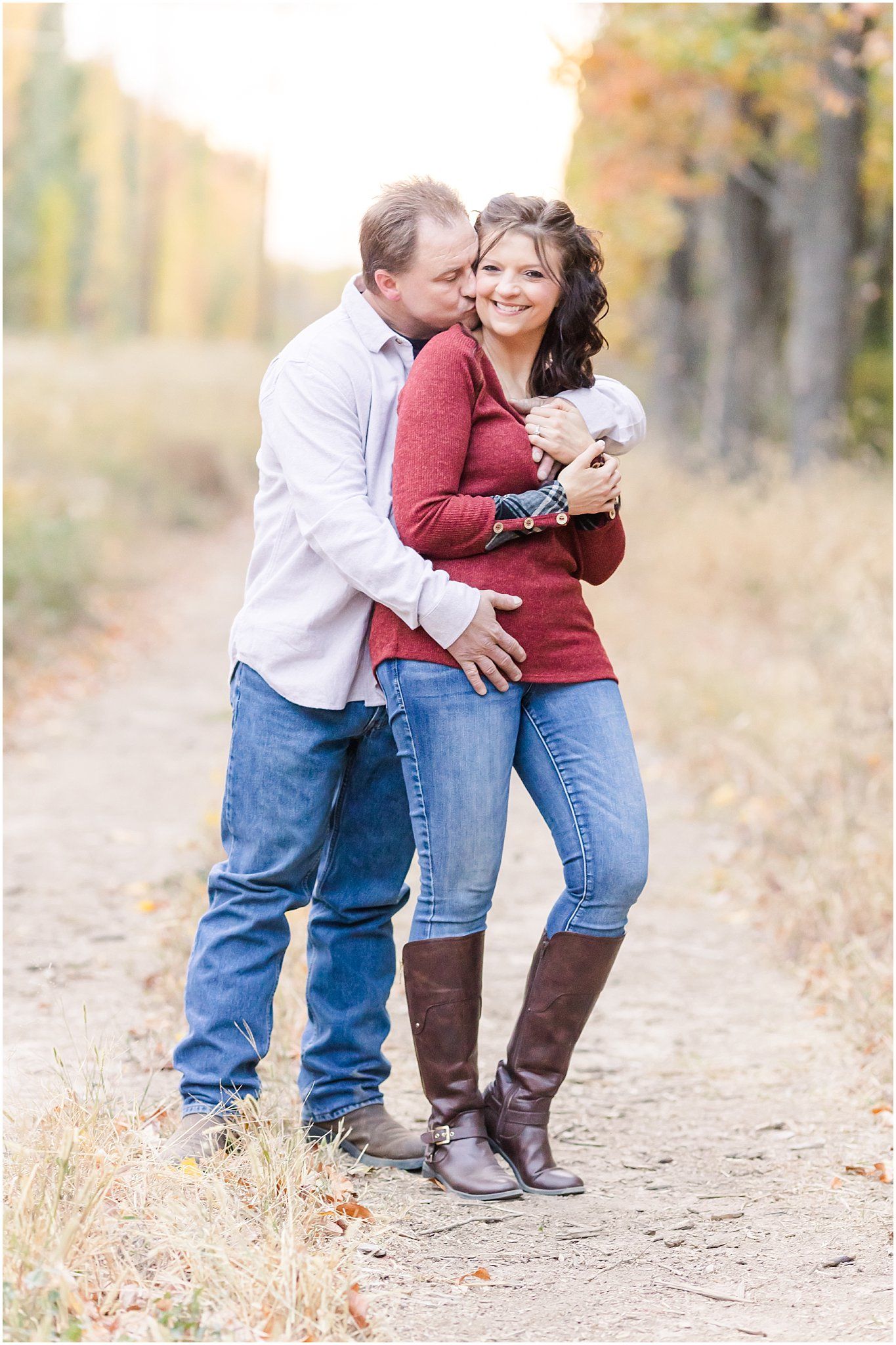 Romantic embrace on dirt trail with autumn trees in background.