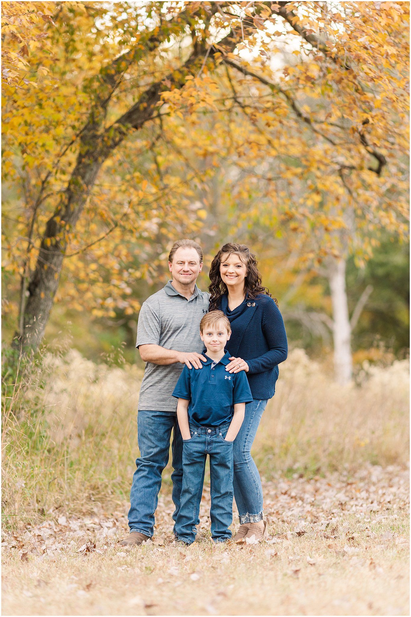 Family standing together under golden autumn tree branches.