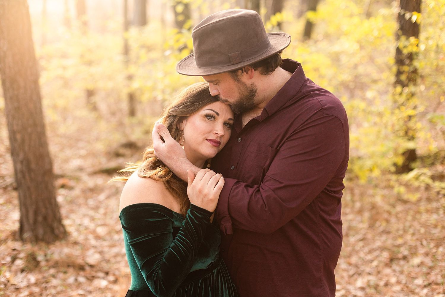 Intimate forest portrait of couple embracing in burgundy shirt and emerald dress.