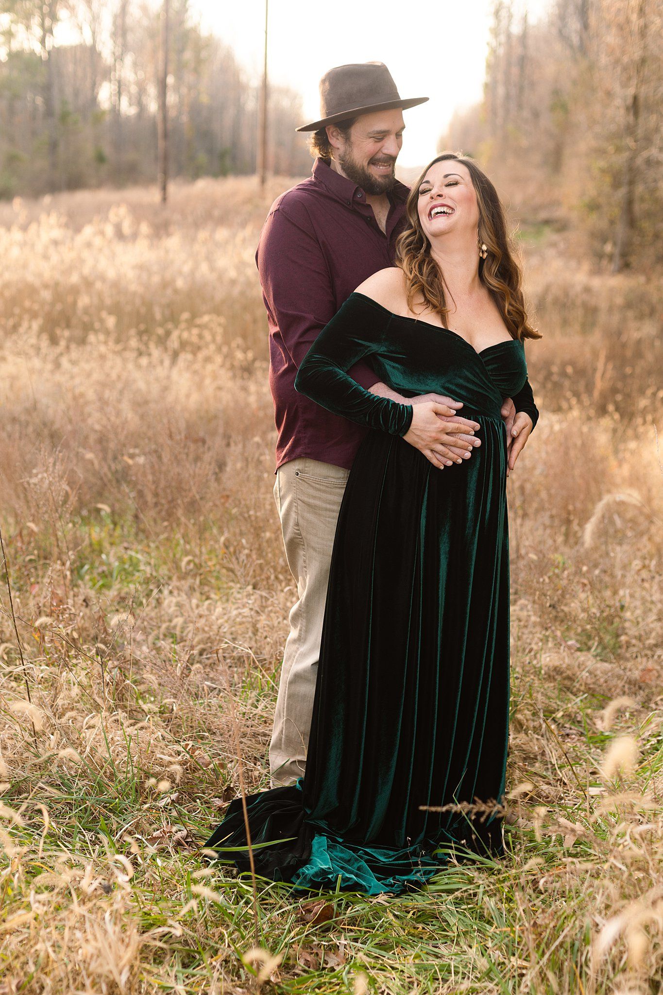 Joyful outdoor maternity portrait with couple laughing in autumn field setting.