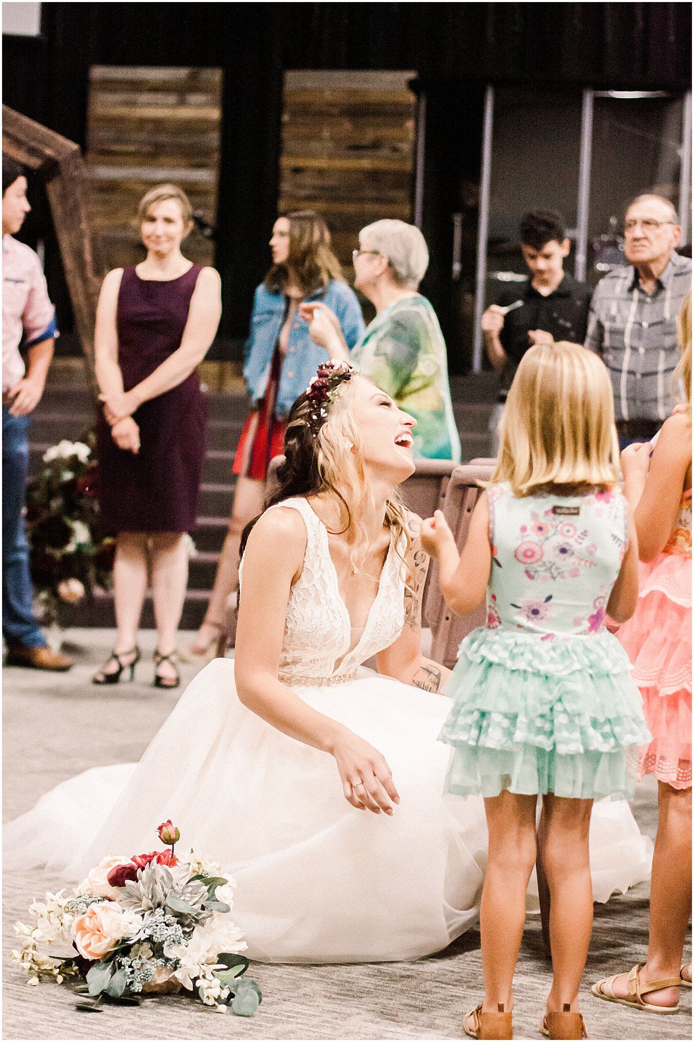 Bride in white gown sitting near decorated steps while interacting with wedding guests.