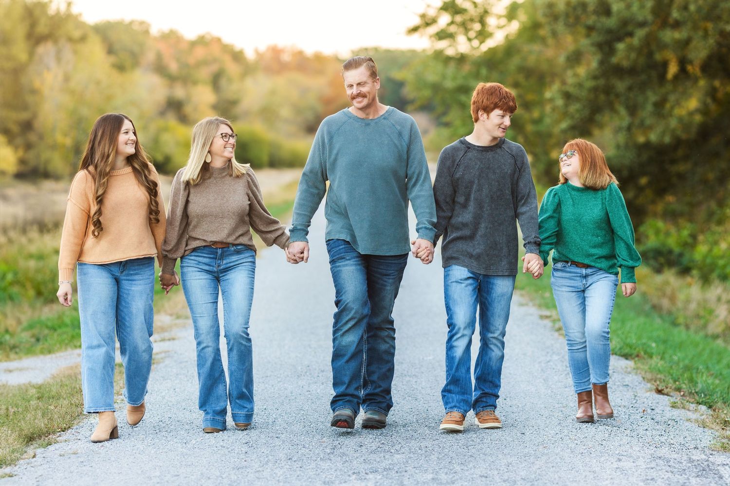 Five people walk hand in hand down a country road during golden hour in autumn.