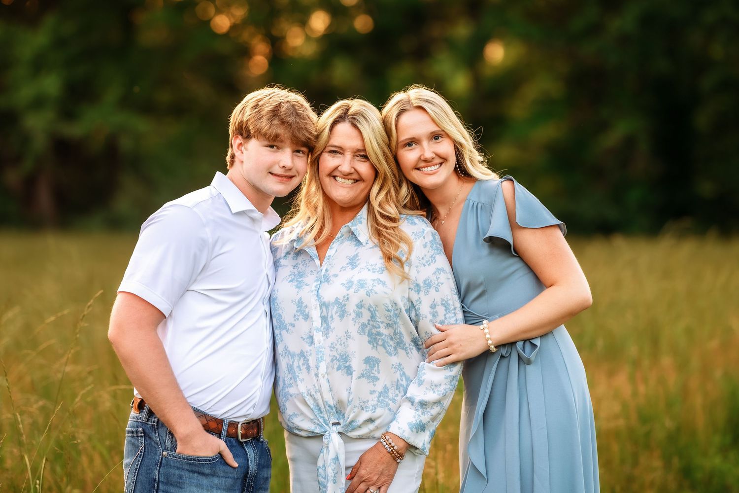 Family members embrace while standing in a sunlit meadow during golden hour.