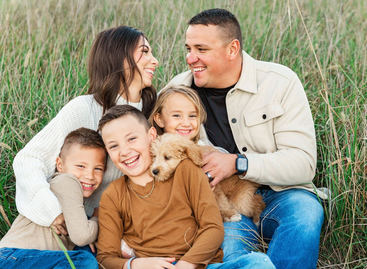 Family shares joyful moment together while sitting in grassy field.