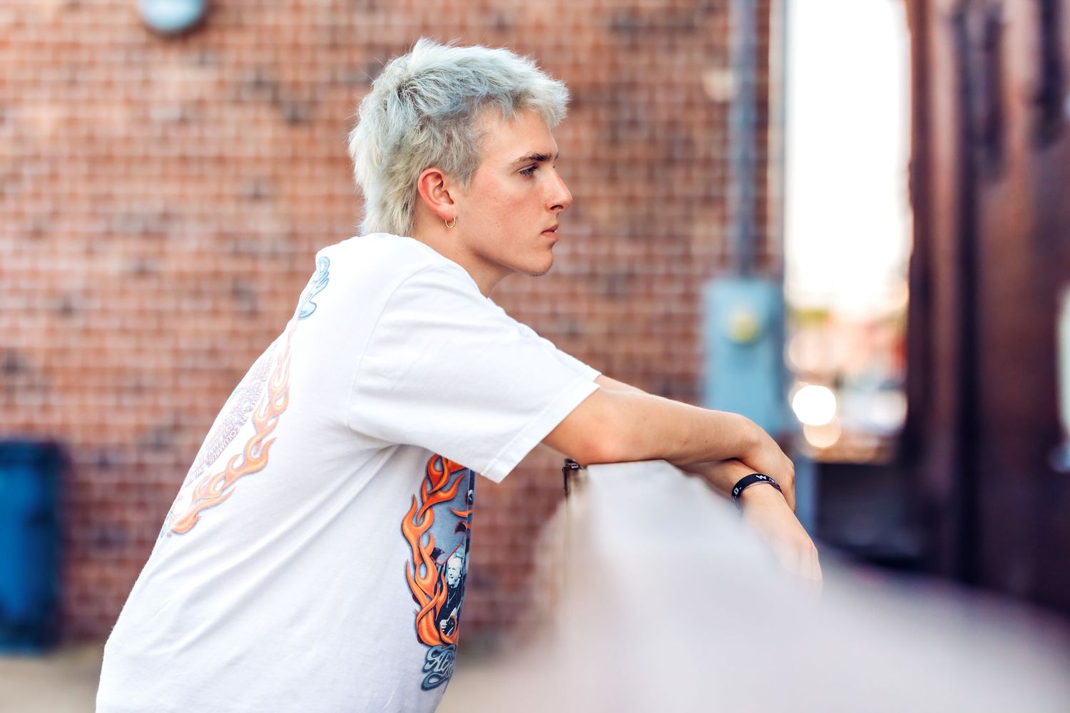 Person in white shirt and jeans poses casually against brick wall background.