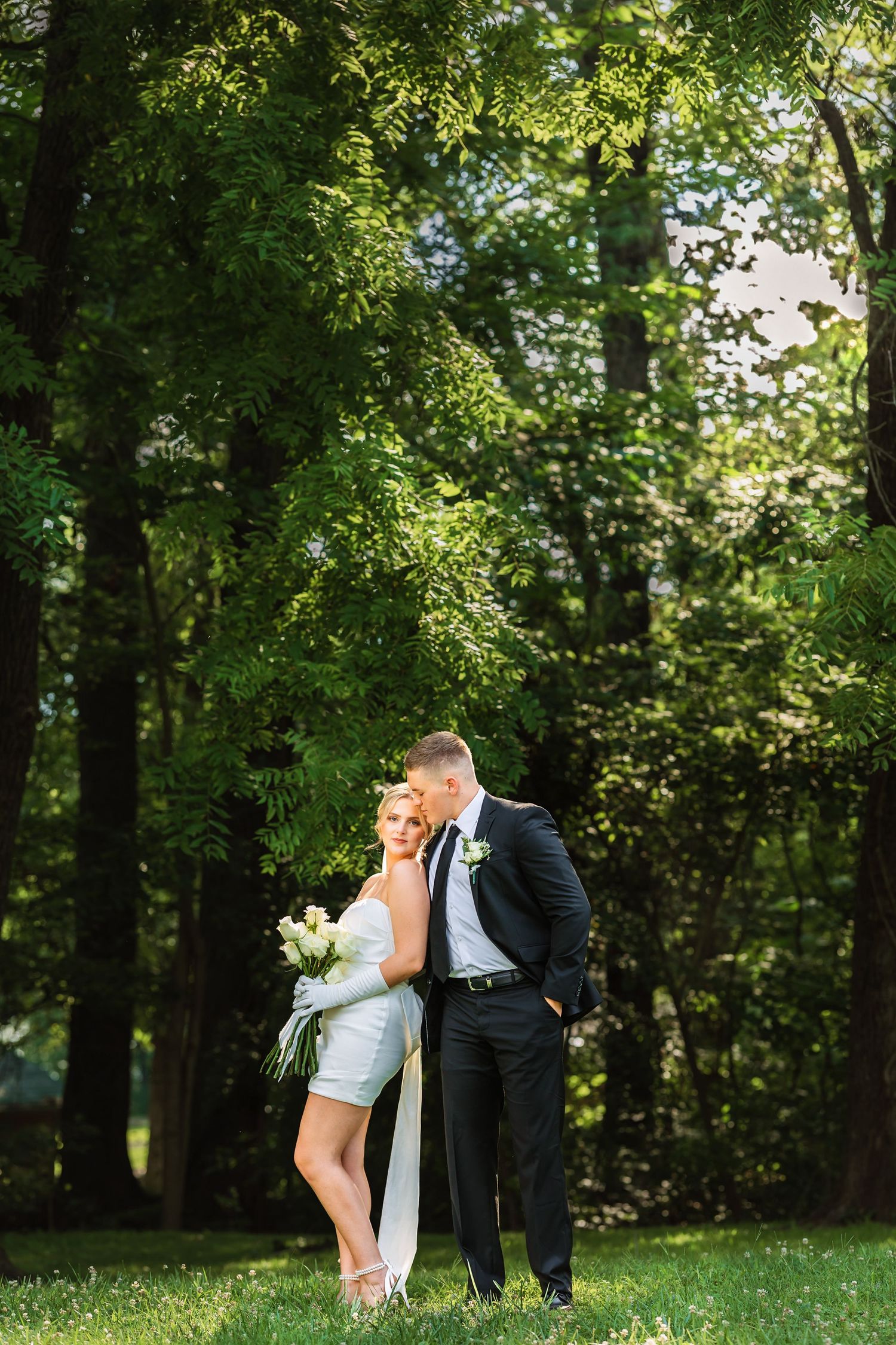 Couple in wedding attire sharing intimate moment in wooded outdoor setting.
