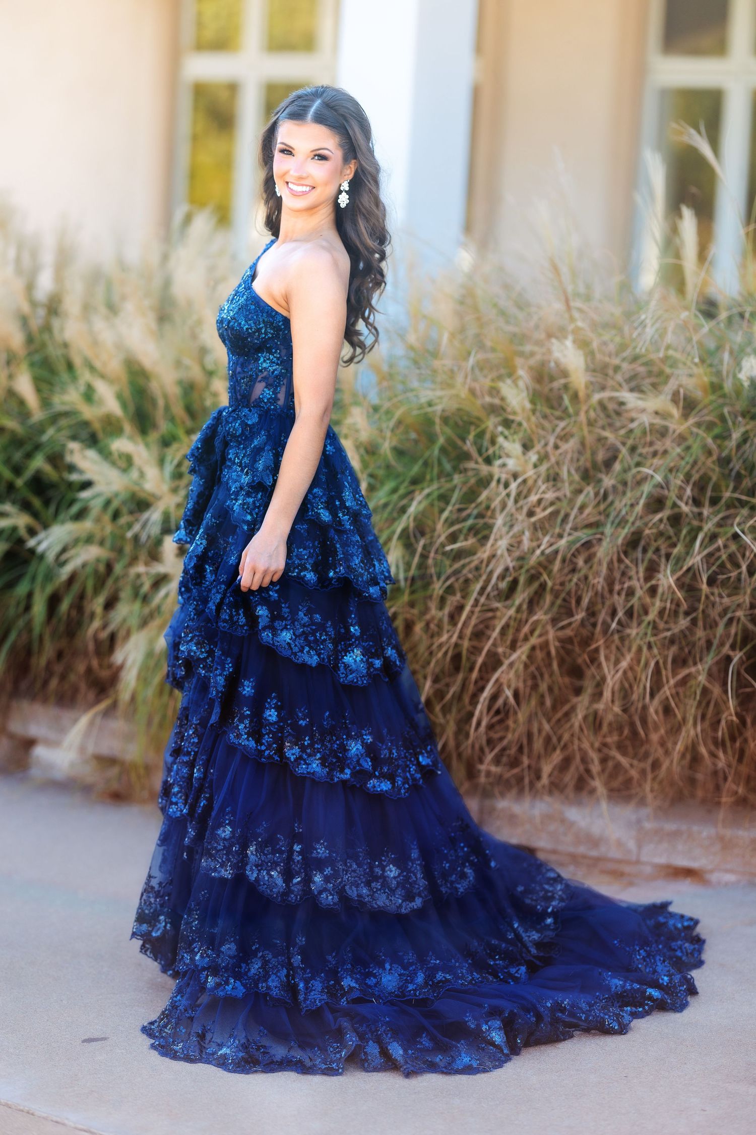 A stunning navy blue tiered lace gown with a flowing train photographed from the side.