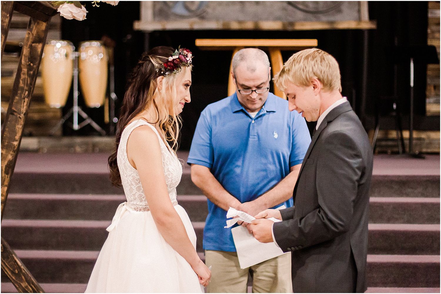 A wedding ceremony takes place on wooden steps with an officiant in blue conducting the service.