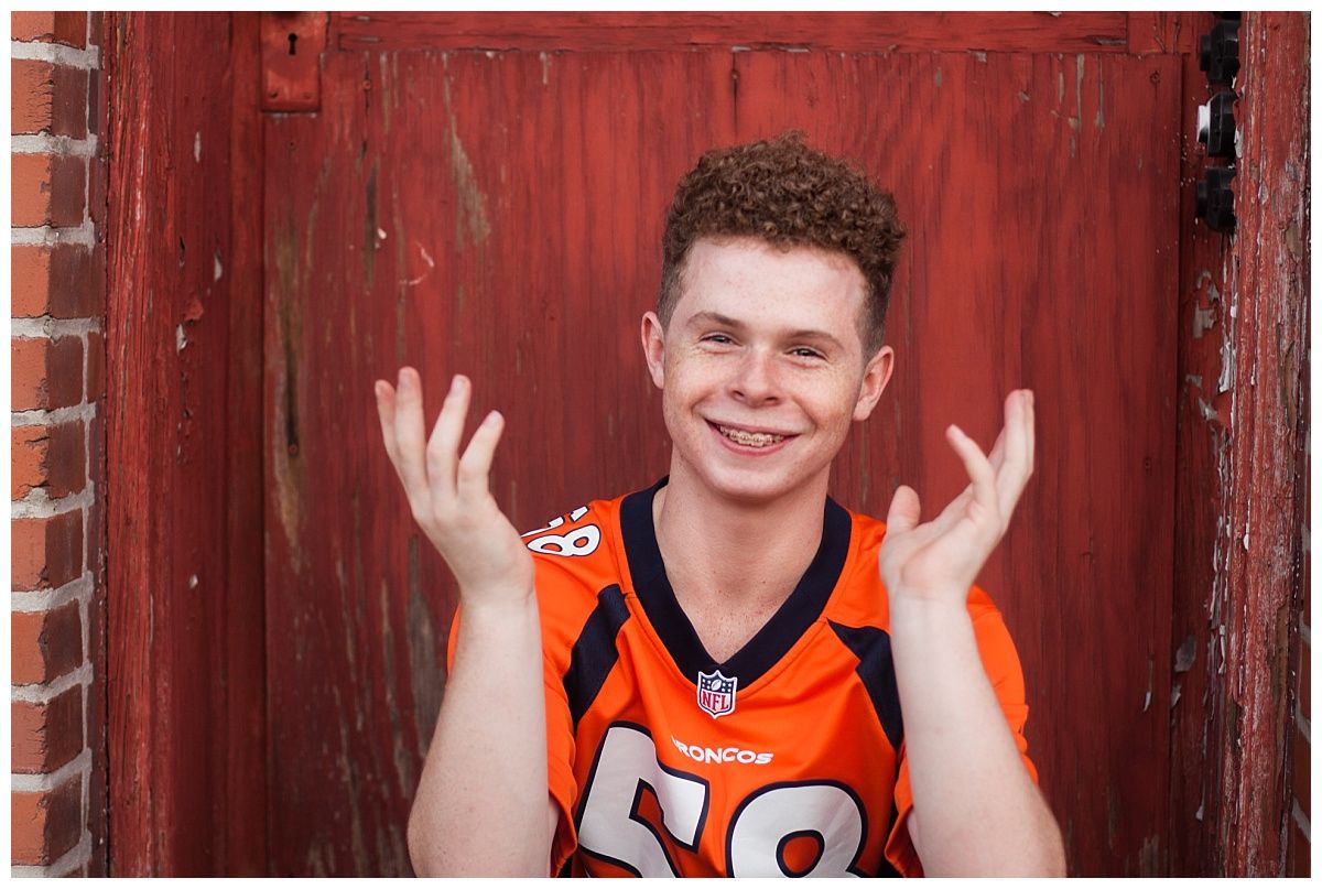 A portrait against a red barn door featuring someone in an orange sports jersey.