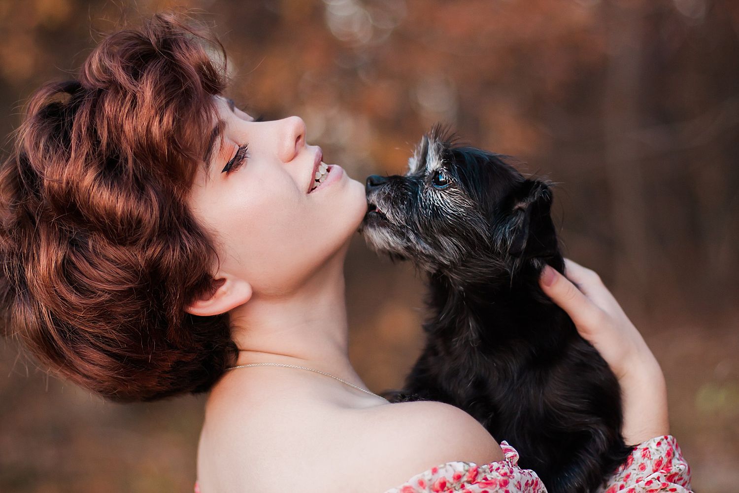 Person with short red hair shares an affectionate moment with a small black dog.